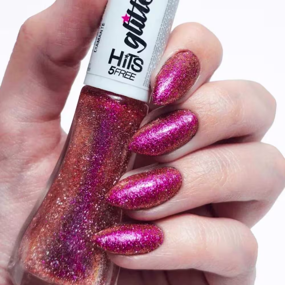 Esmalte glitter rosa e dourado da marca Hits 5Free. Frasco de esmalte com tampa branca e rótulo preto com o nome da marca e linha de produto. As unhas pintadas mostram um acabamento brilhante e cintilante com tons de rosa vibrante e dourado metálico.