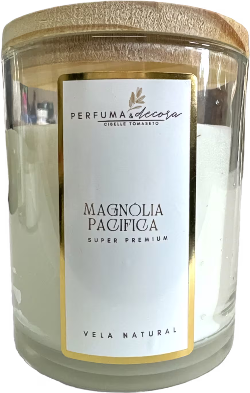 Vela natural em frasco de vidro transparente com tampa dourada. A embalagem tem um rótulo branco com o nome "Magnolia Pacifica Super Premium" em letras pretas e o logotipo "Perfuma & Decora" em dourado.