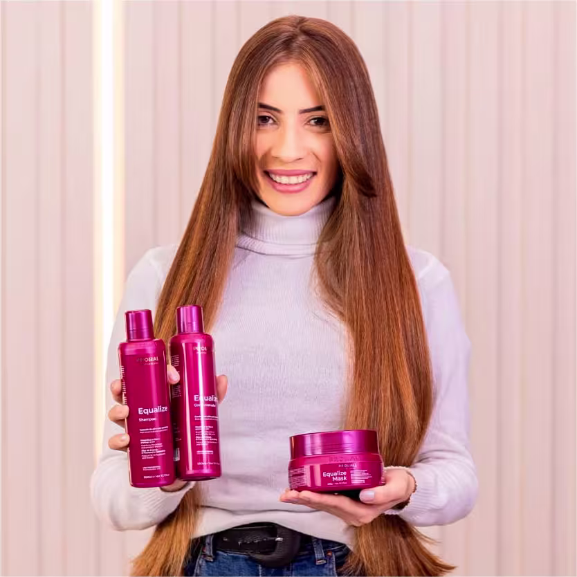 A imagem mostra uma mulher segurando produtos da linha Equalize, sendo um shampoo, um condicionador e uma máscara.