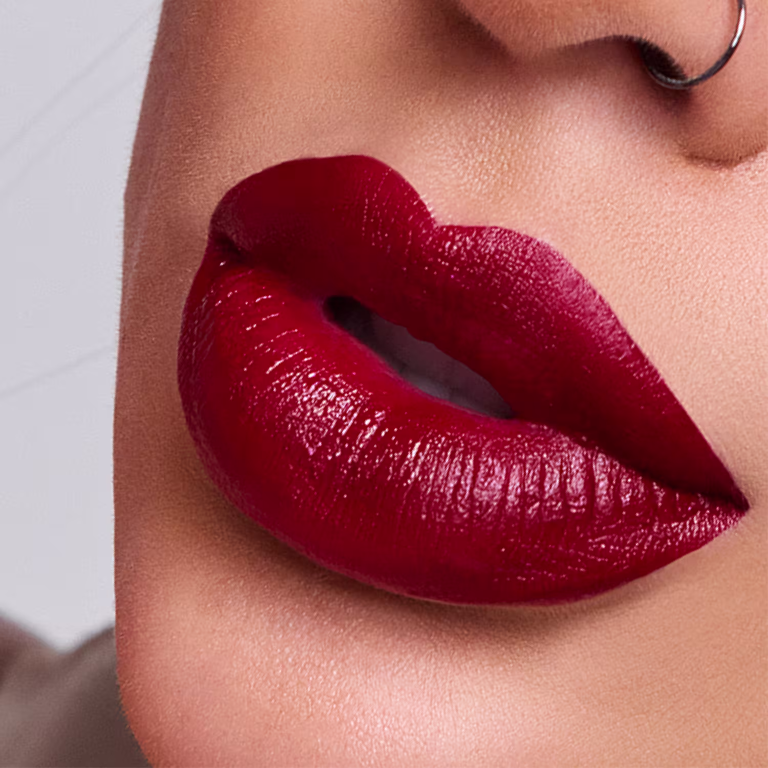 A imagem mostra um close em uma boca feminina com batom vermelho intenso e brilhante aplicado nos lábios. Os lábios estão entreabertos, exibindo uma maquiagem impecável e sedutora.