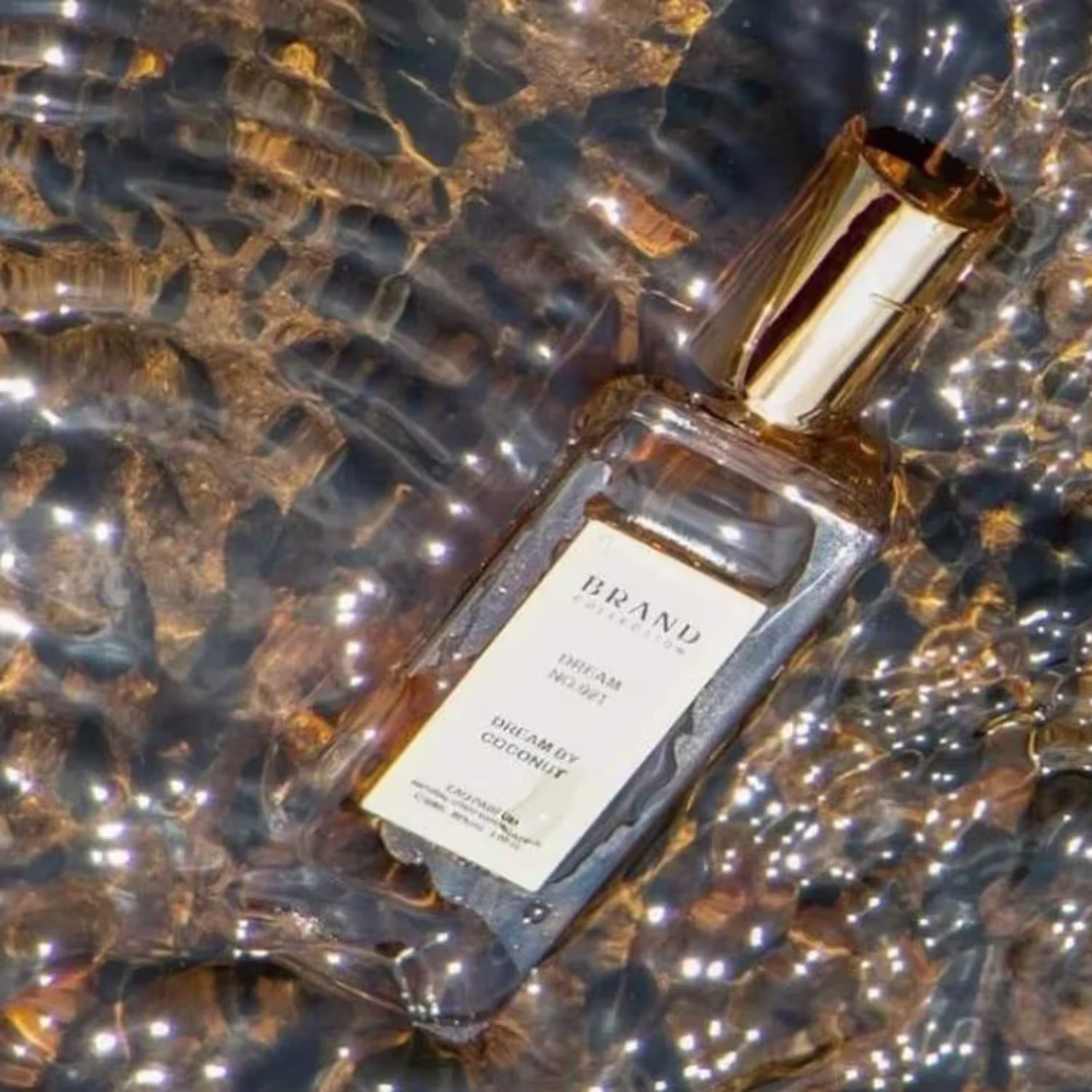 A imagem mostra o frasco do perfume submergindo em uma superfície de água com um fundo de pedras marrons, lembrando um rio.
