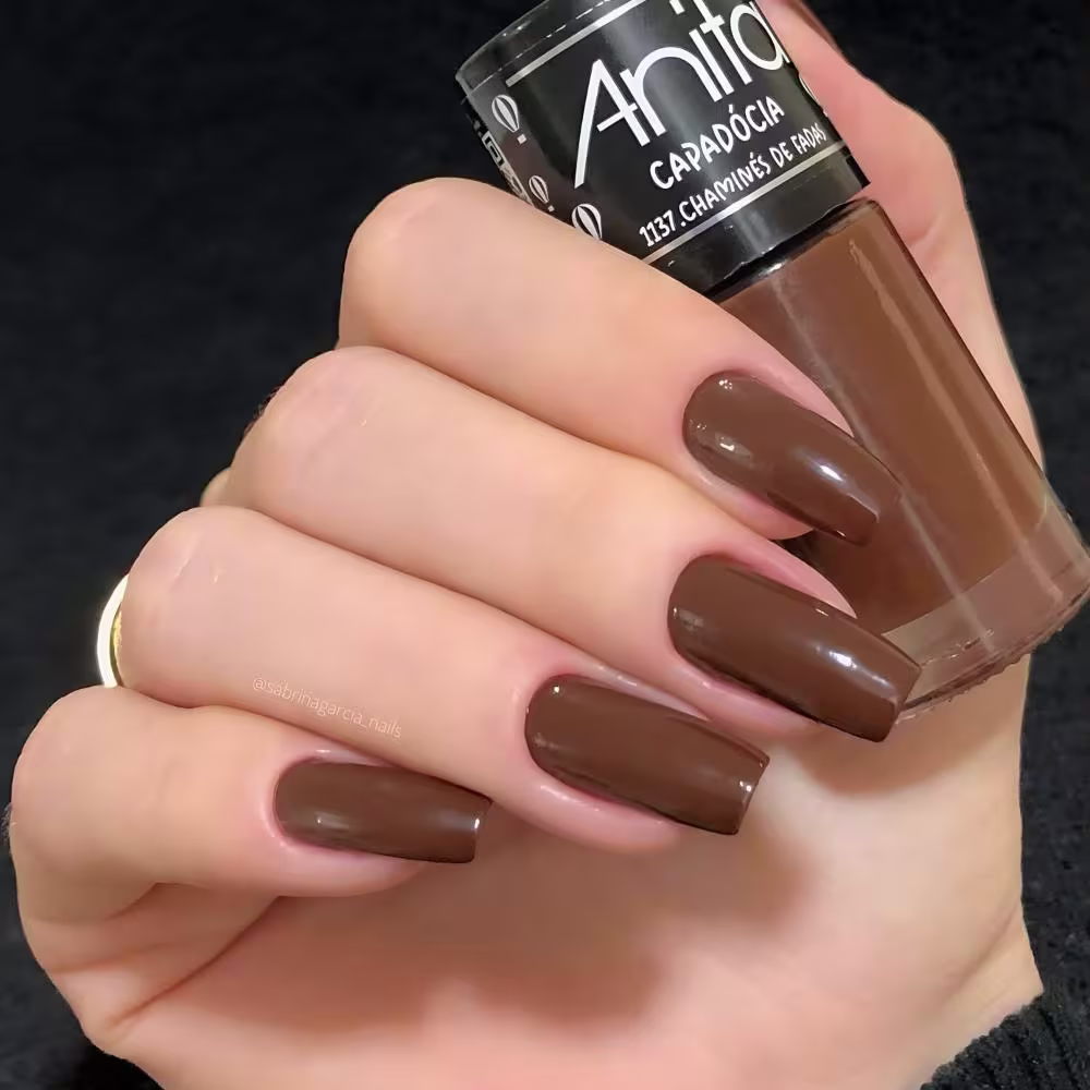 Modelo segurando o frasco de esmalte com suas unhas pintadas da mesma cor.