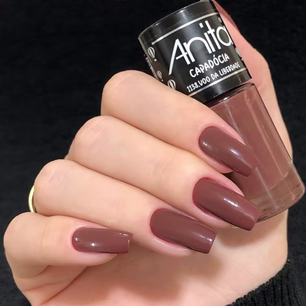 Modelo segurando o frasco de esmalte com suas unhas pintadas da mesma cor.