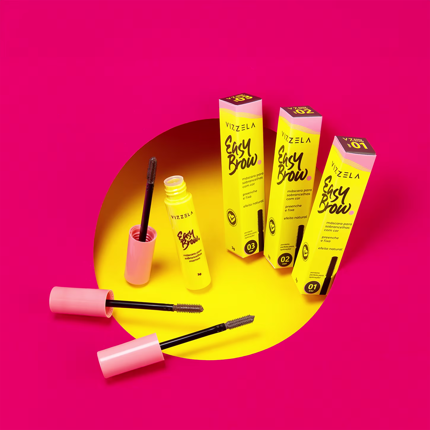 Produtos de maquiagem para sobrancelhas da marca Vizzela. Embalagens retangulares em tons de amarelo e rosa, com o nome do produto "Easy Brow" e a descrição "máscara para sobrancelhas com cor" em letras estilizadas.