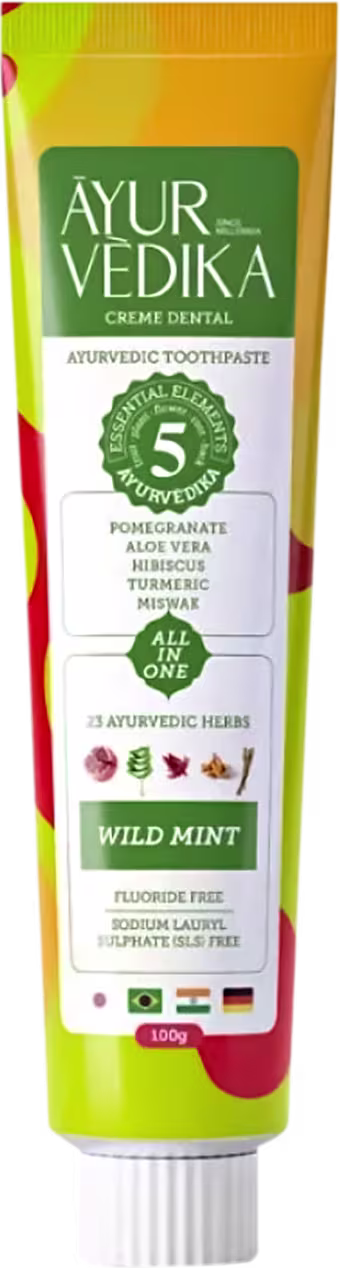 Creme dental Ayurvédico da marca AyurVedika. A embalagem é um tubo de cor amarela e verde, com rótulo destacando os ingredientes naturais como romã, aloe vera, hibisco e curcuma. O texto indica que o produto é livre de flúor e contém 25 ervas ayurvédicas.