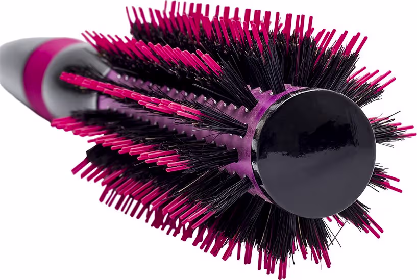 A imagem mostra a escova de cabelo em formato arredondado. Ela possui um corpo preto com cerdas rígidas e densas em tons de rosa vibrante e preto. Design moderno e ergonômico com cabo emborrachado rosa.