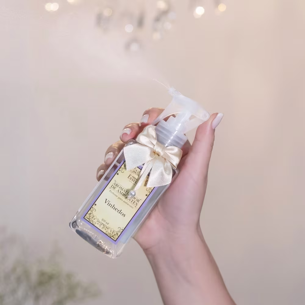 Frasco de vidro transparente com rótulo dourado e laço branco, contendo um produto de beleza da marca Empório Essenza Serra Gaúcha, chamado Vinhedos.