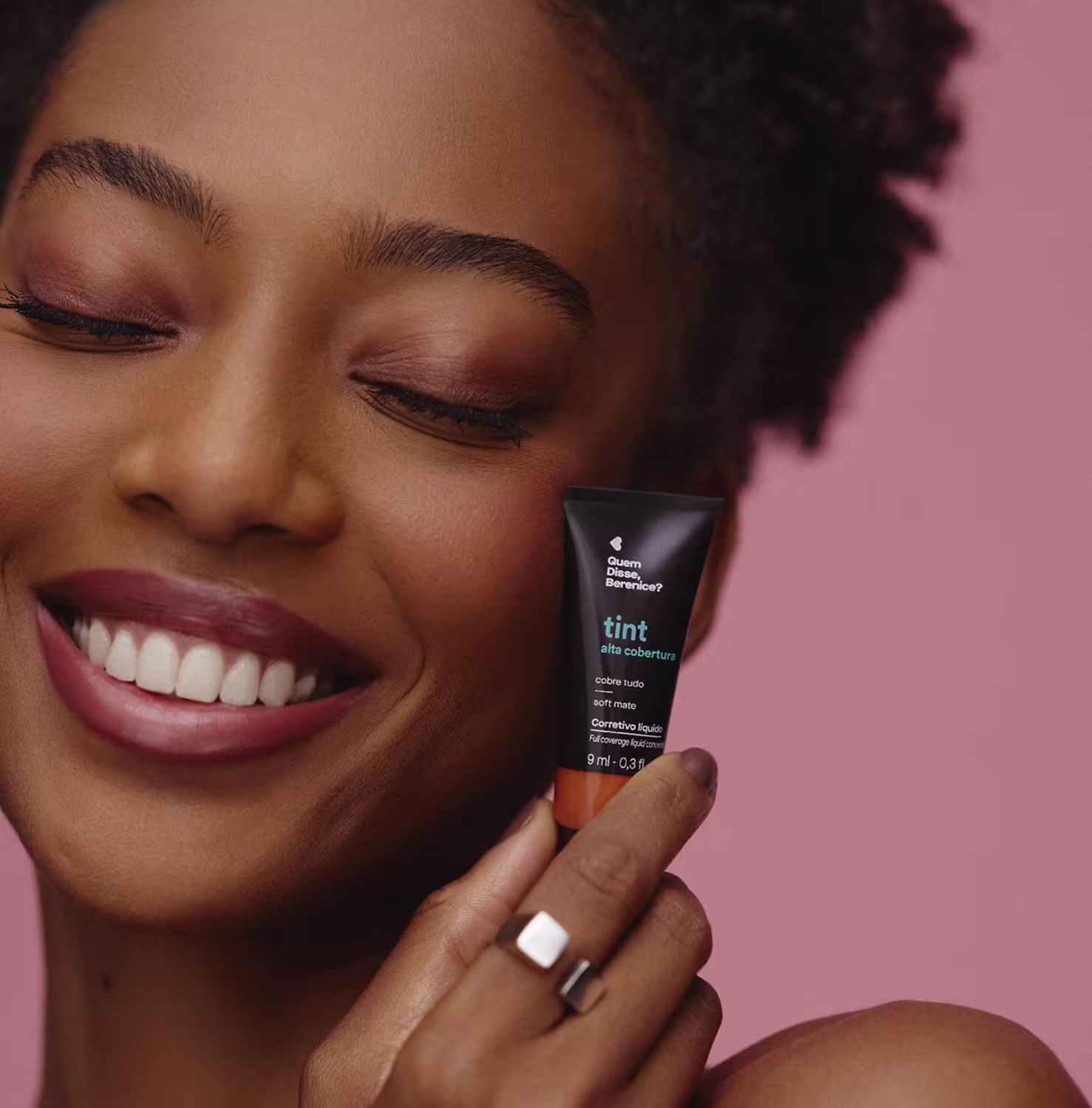 Imagem mostra uma mulher negra segurando o corretivo próximo ao seu rosto e sorrindo.