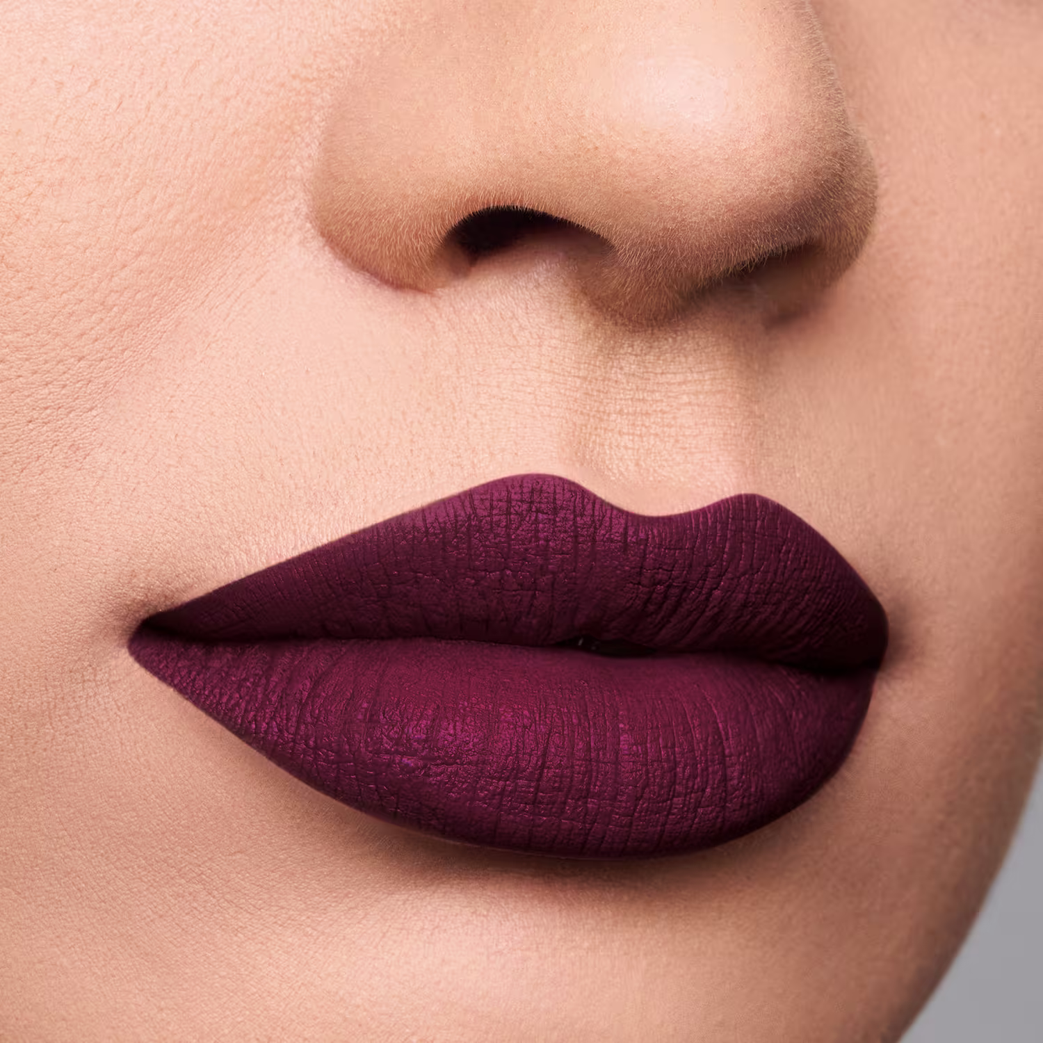 A imagem mostra um close-up dos lábios de uma pessoa, com uma maquiagem de batom de cor vinho escuro. O batom tem uma textura cremosa, criando um visual elegante e sofisticado.