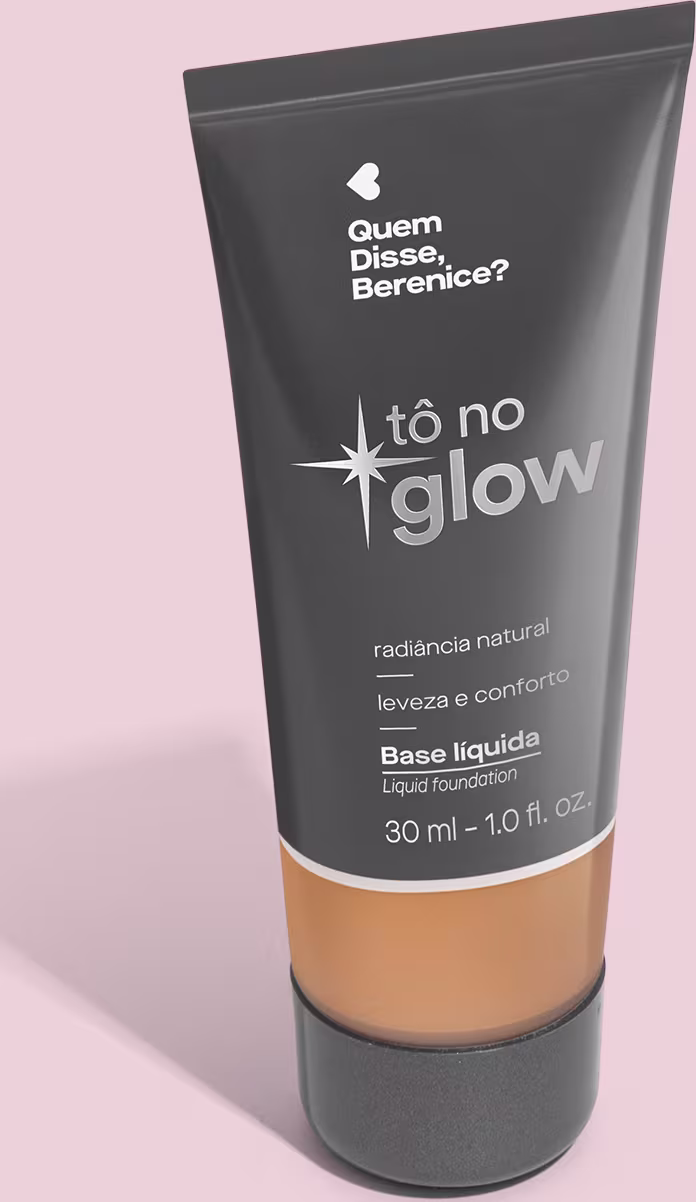 Base líquida em bisnaga preta com base transparente onde é possível ver o tom do produto. Fundo rosa.