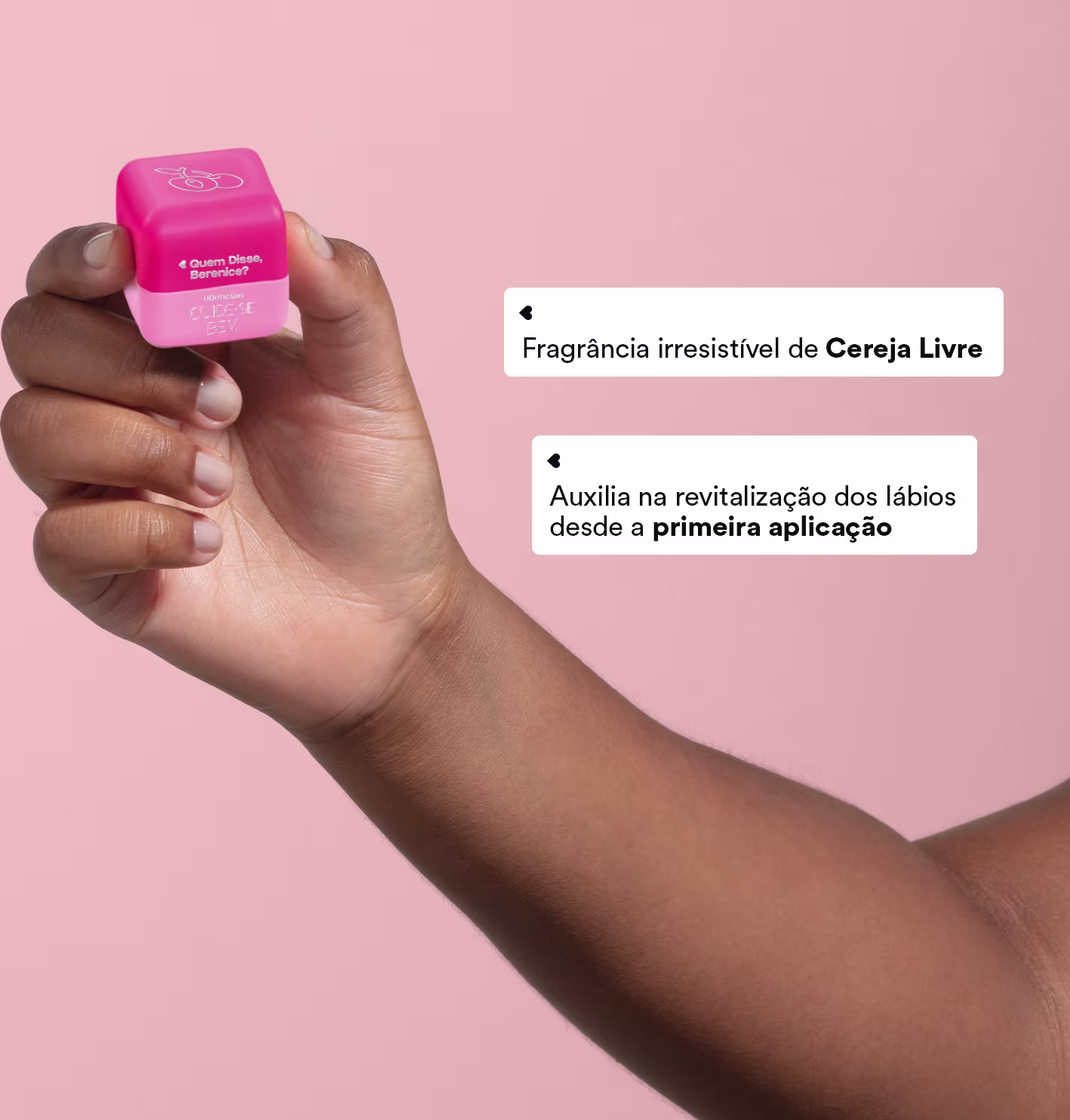 A imagem mostra uma mão segurando o hidratante labial Quem Disse, Berenice? Cuide-se Bem Cereja Livre o Boticário em um fundo rosa. Ao lado aparece o texto: "Fragrância irresistível de Cereja Livre" e "Auxilia na revitalização dos lábios".