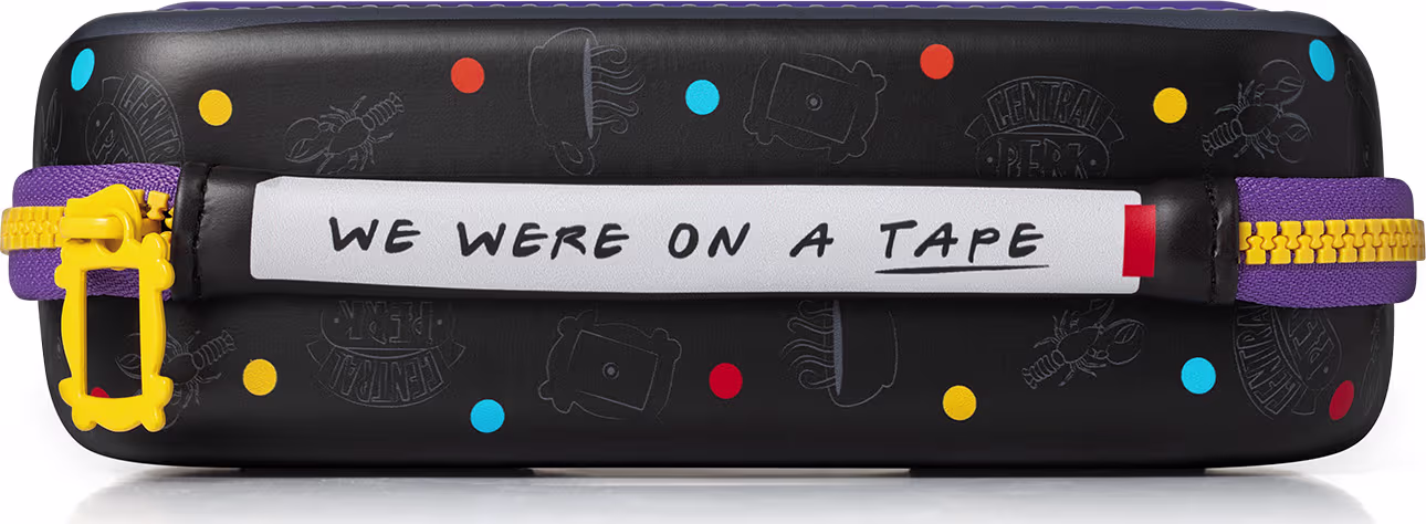 Bolsa preta com estampas coloridas de câmeras, fitas e outros símbolos. Texto "We were on a tape" escrito na parte frontal. Objeto de uso pessoal ou de viagem com design divertido e informal.