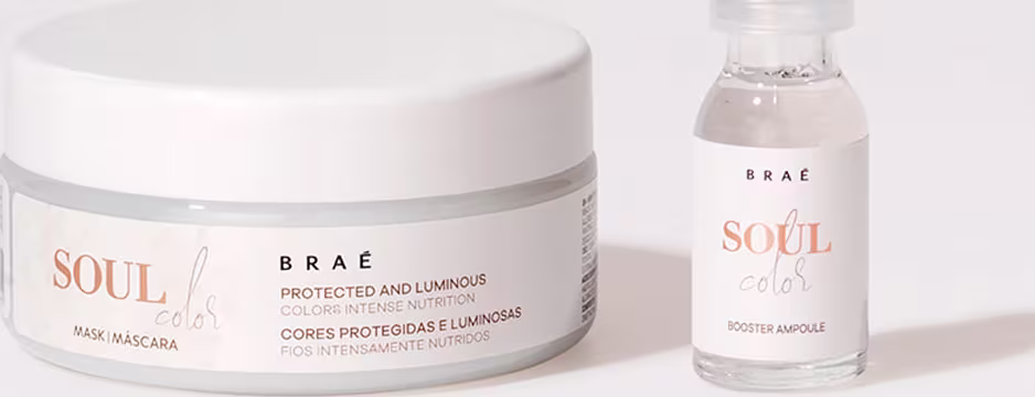 A imagem mostra dois produtos da linha Soul da marca Braé. Um é uma máscara capilar em um pote branco com a inscrição "Soul Color" e detalhes em laranja. O outro é uma ampola em um frasco transparente, também com o nome "Soul Color" e detalhes em laranja.