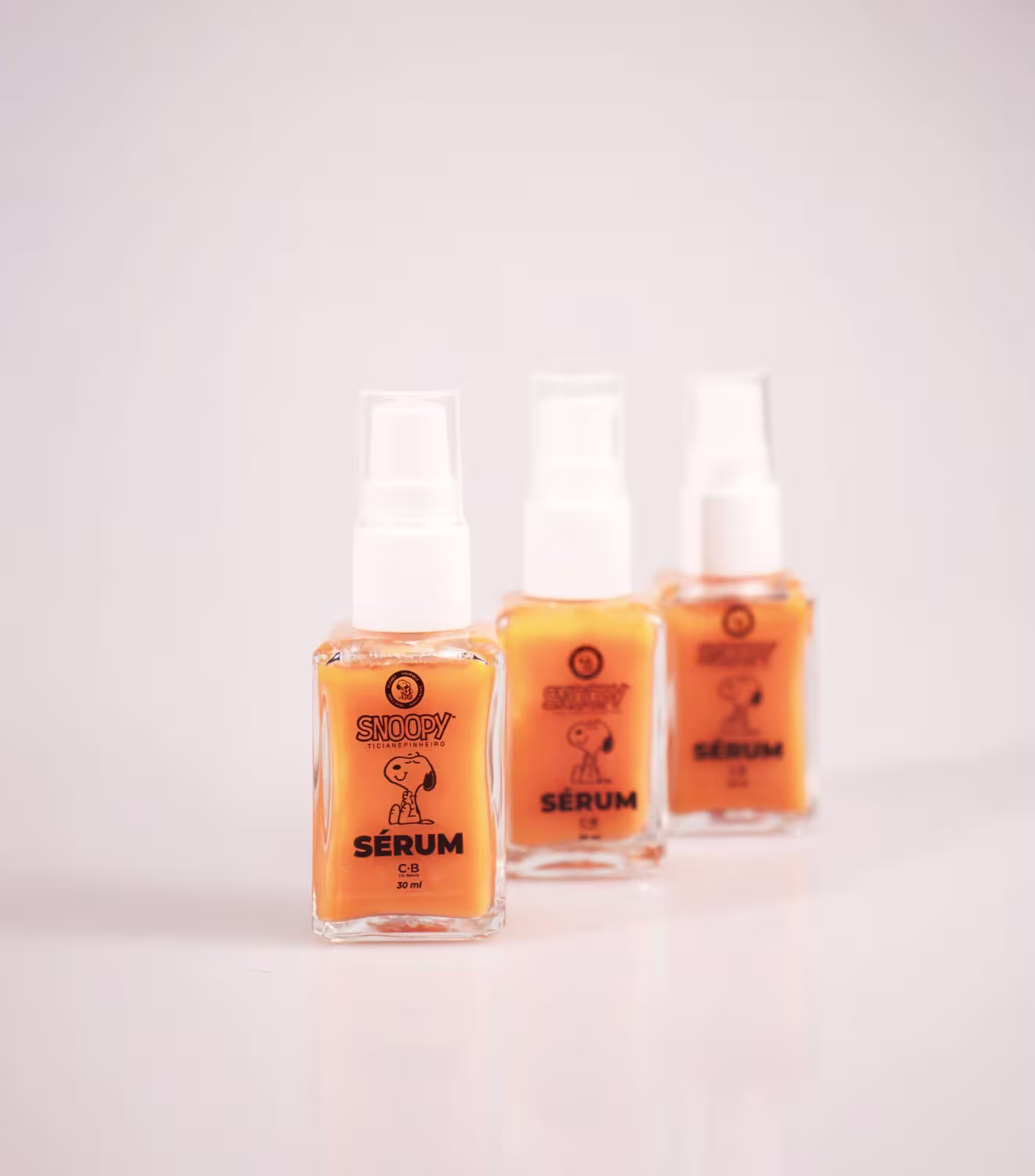 A embalagem possui uma cor laranja predominante, com o logotipo da marca Snoopy impresso em preto. Cada frasco contém 30 ml do produto.