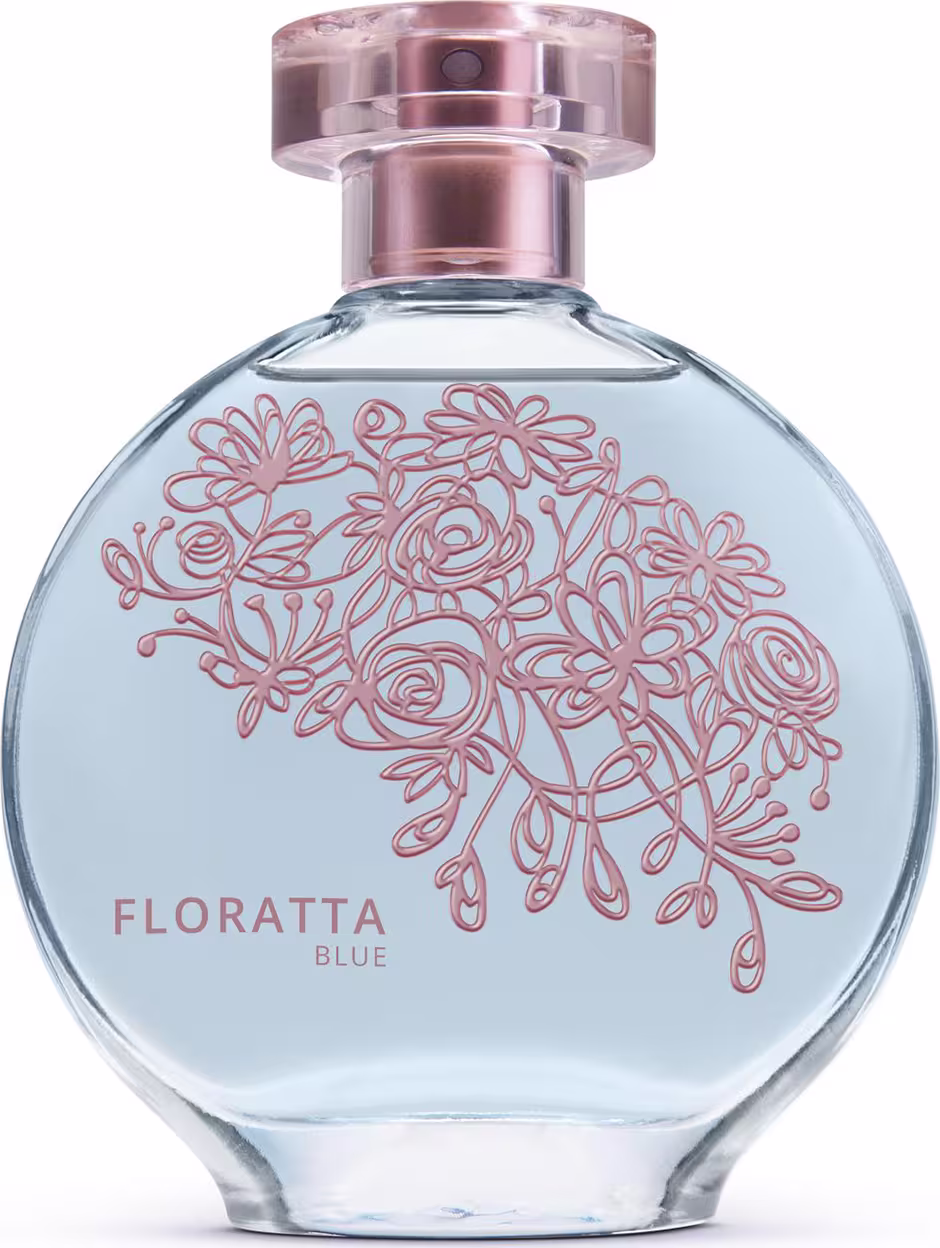 A imagem mostra um frasco de perfume da linha Floratta Blue. O frasco é de vidro transparente com um design arredondado. Há um padrão floral estilizado em tons de rosa desenhado sobre o fundo azul claro do frasco. A tampa é cor de rose gold metálico.