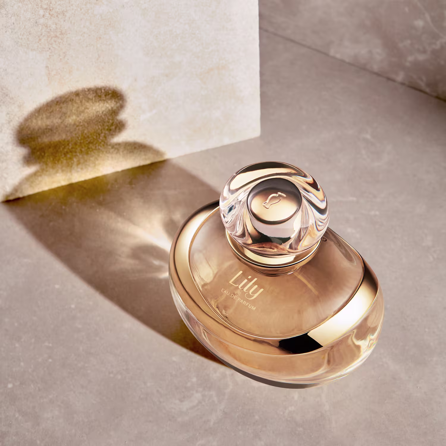 A imagem mostra um frasco de perfume da marca Lily. Ao lado do frasco, há uma projeção de sombra na superfície bege, dando um toque suave e elegante à cena.