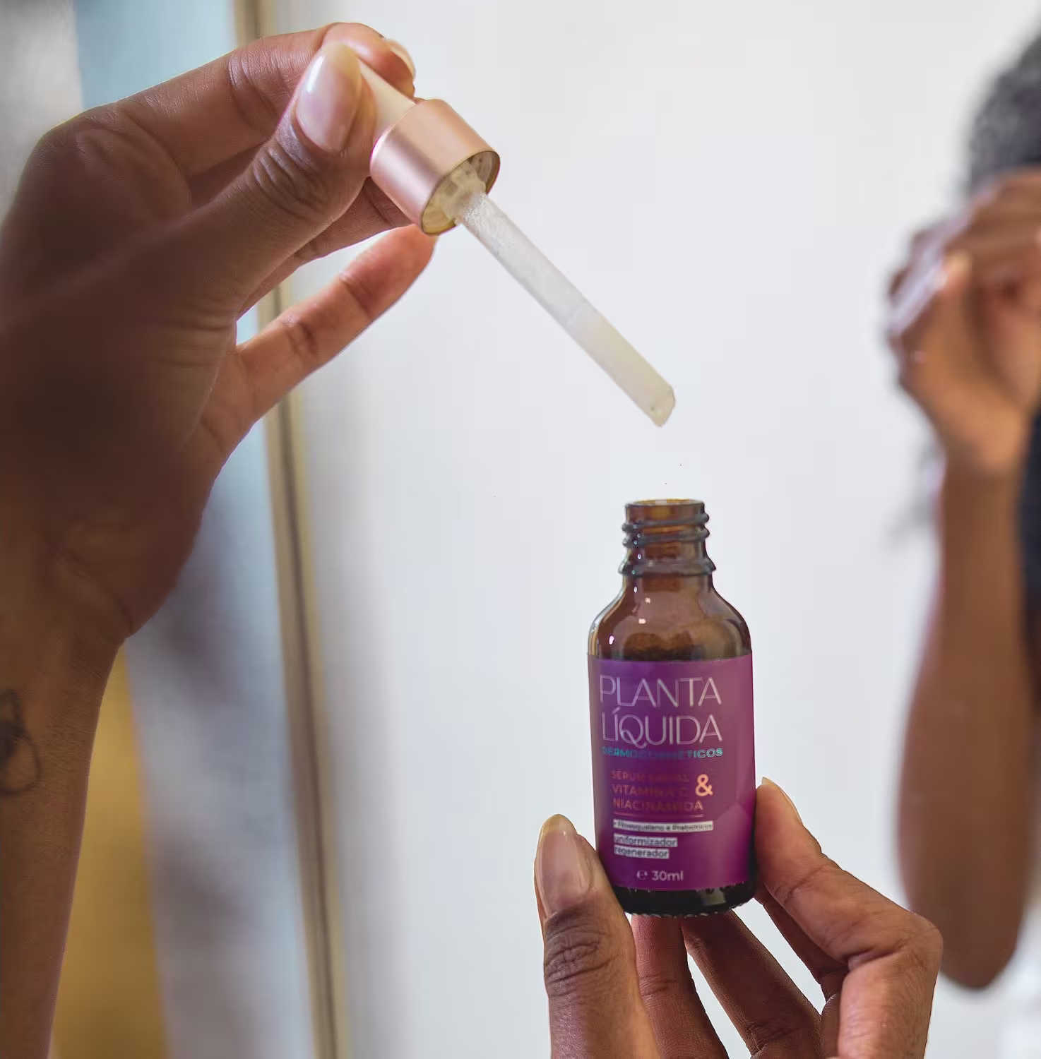 A imagem mostra mãos segurando uma pipeta e um frasco de um produto líquido da marca "Planta Liquida". O frasco é de cor roxa e tem o rótulo indicando que é um sérum facial.