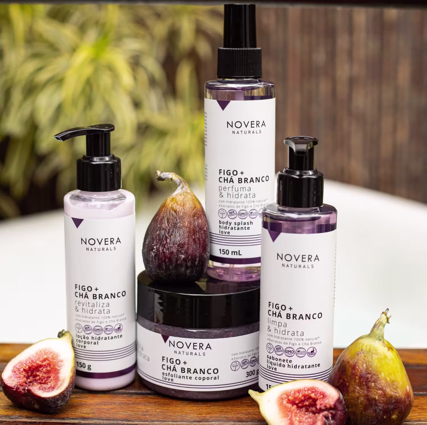 A imagem mostra várias embalagens de tamanhos diferentes, transparentes, com detalhes em roxo e preto. São potes de hidratante corporal, loção hidratante e um esfoliante corporal. Ao lado deles, há figos frescos cortados ao meio.
