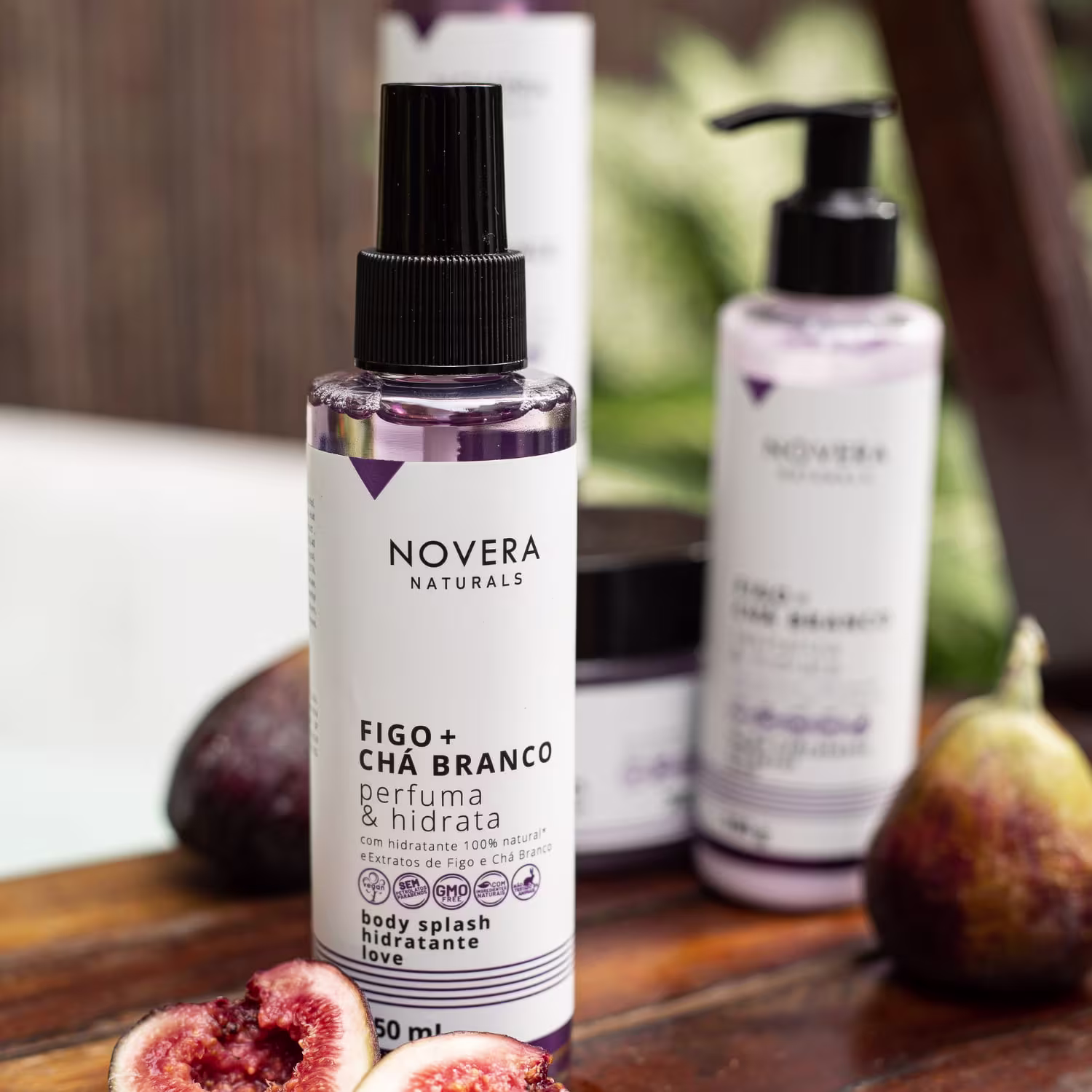 A imagem mostra body splash Novera Naturals Figo + Chá Branco. O frasco é transparente, tem 150ml de capacidade e está acompanhado de alguns figos ao redor e posicionado sobre uma superfície de madeira.