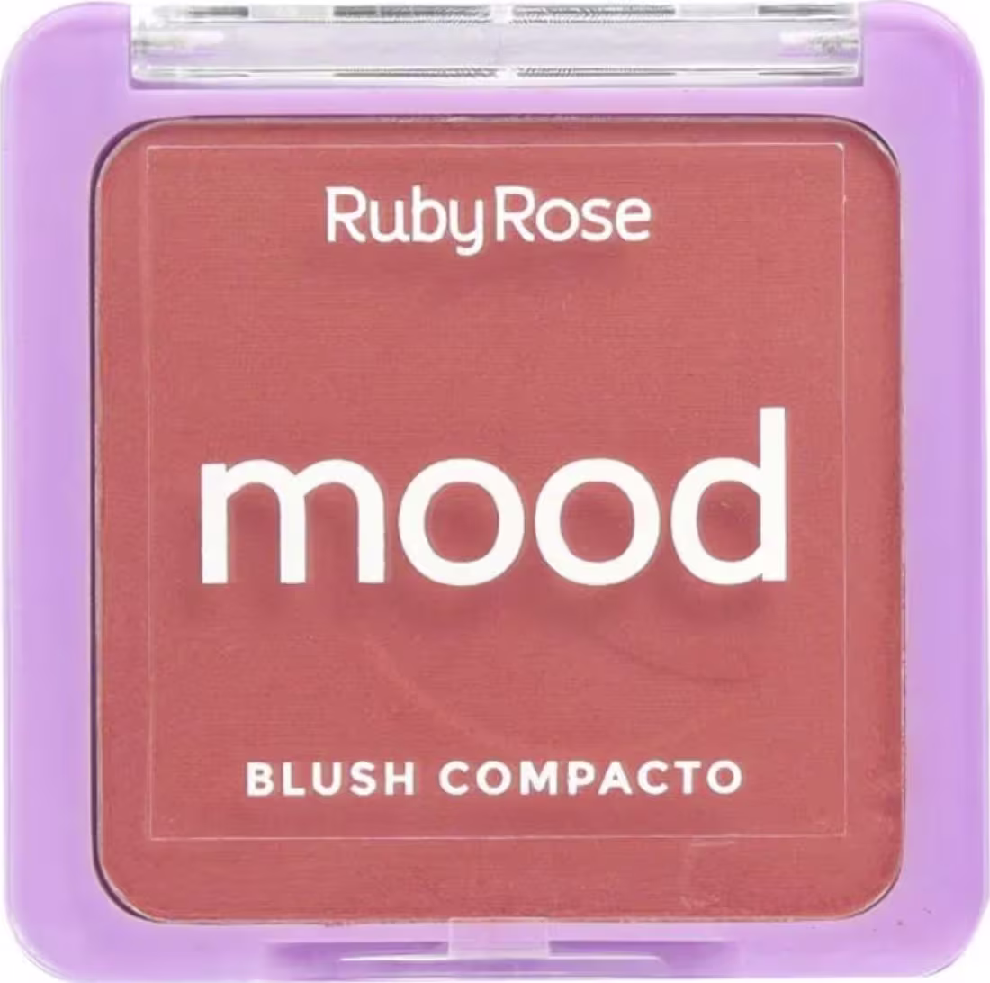 Blush compacto da marca Ruby Rose, com a palavra "mood" impressa na embalagem. A embalagem é retangular, com uma tampa transparente que permite visualizar o conteúdo. A cor predominante da embalagem é um tom de roxo claro.