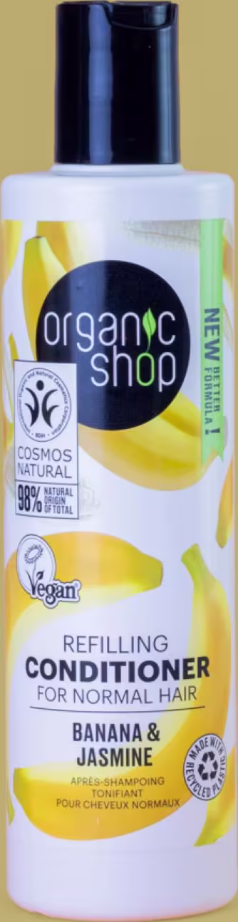 A imagem mostra o condicionador em embalagem plástica transparente com tampa preta. Rótulo branco com imagens de bananas e flores de jasmim em amarelo.