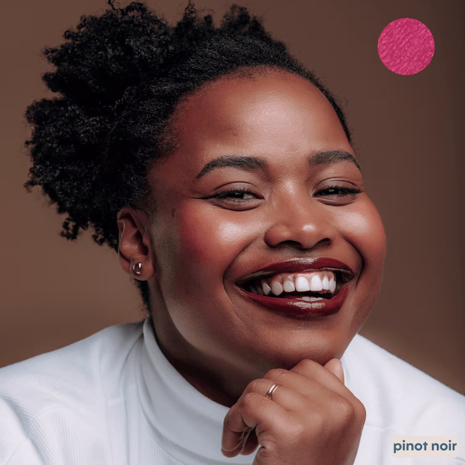 A imagem mostra uma mulher sorrindo com expressão alegre. Ela está maquiada com batom marrom e blush na cor pinot noir
