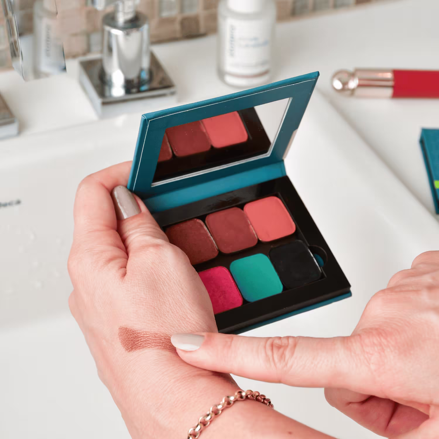 O produto mostrado na imagem é uma paleta de sombras de olhos da marca Statera. A paleta possui um design retangular com uma estrutura em tons de azul escuro. Dentro da paleta, há seis sombras em diferentes tons de vermelho, rosa e turquesa
