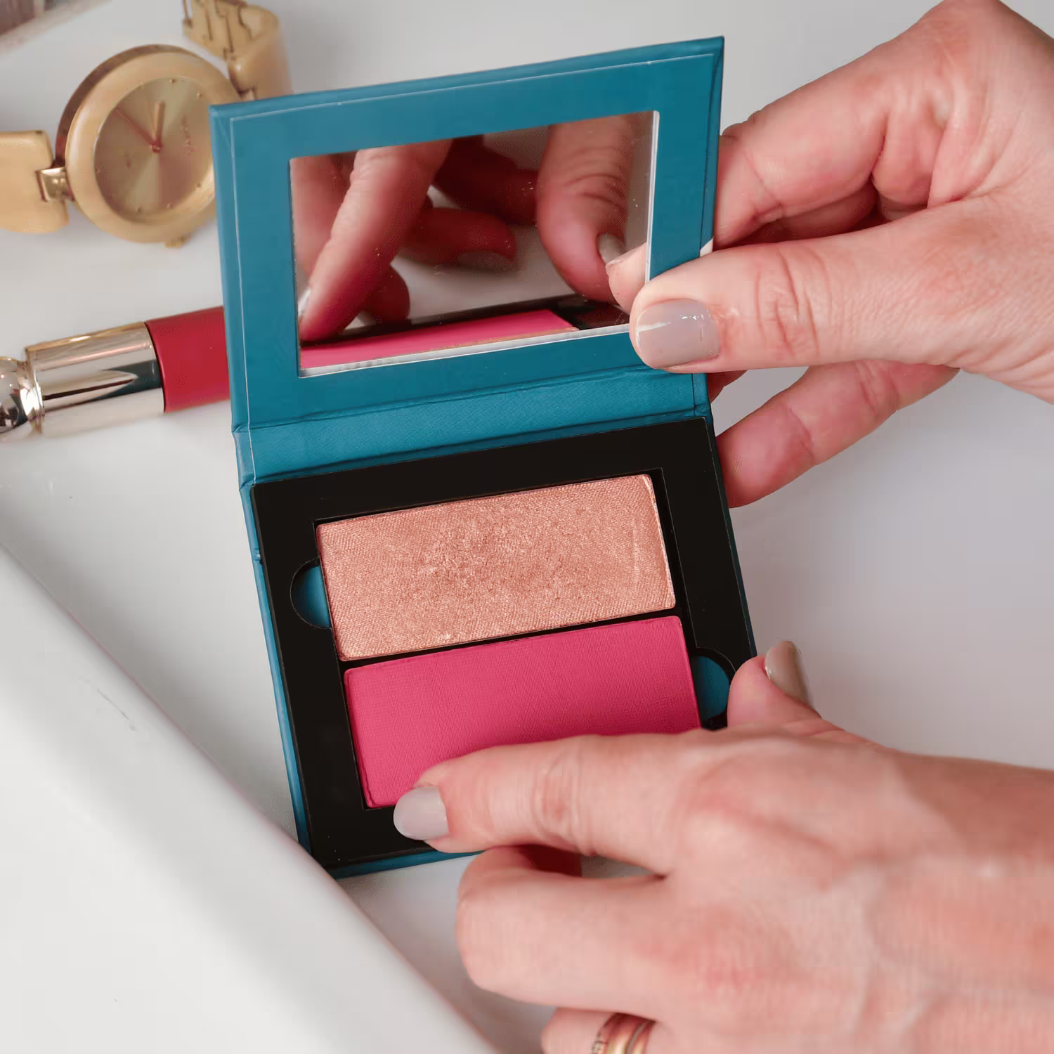 O produto mostrado na imagem é uma paleta de maquiagem da marca Statera. A paleta possui um design compacto com uma caixa de cor azul turquesa. Dentro da caixa, há dois compartimentos com sombras em tons de rosa e dourado.
