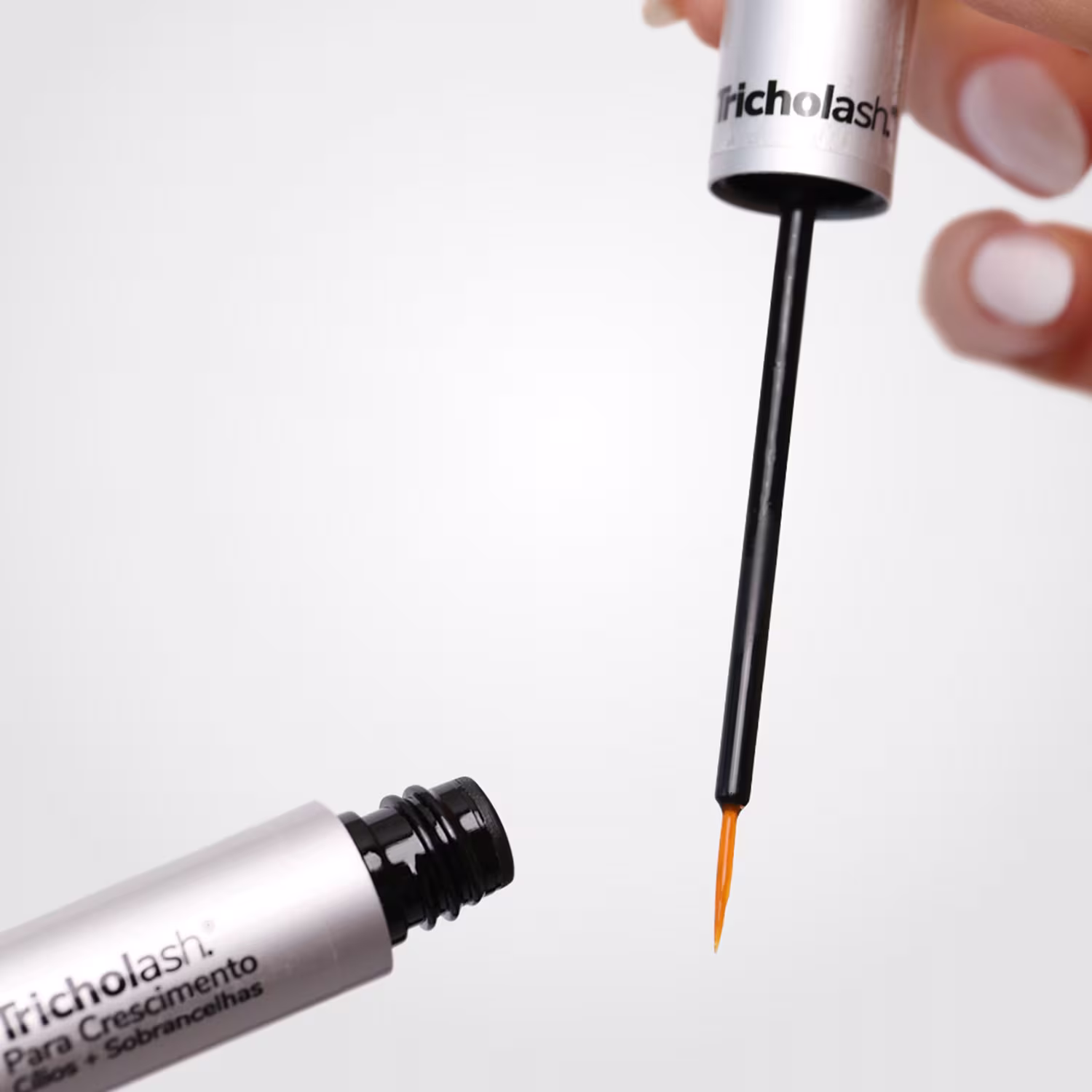 O aplicador possui um tubo preto com uma ponta fina e escura, provavelmente para aplicar o produto com precisão. O rótulo do produto está visível, indicando que se trata de um "Tricholash" para crescimento de cílios.
