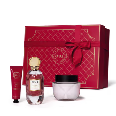 Conjunto. A peça central é o frasco do perfume em vidro transparente com líquido rosa claro e detalhes dourados na tampa e rótulo. Acompanha creme em embalagem redonda de vidro transparente, um frasco tubo vermelho de creme para mãos e caixa de presente