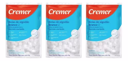 Três pacotes de bolas de algodão branco da marca Cremer, com rótulos em laranja e azul indicando o produto. Cada pacote contém peso líquido de 99g.