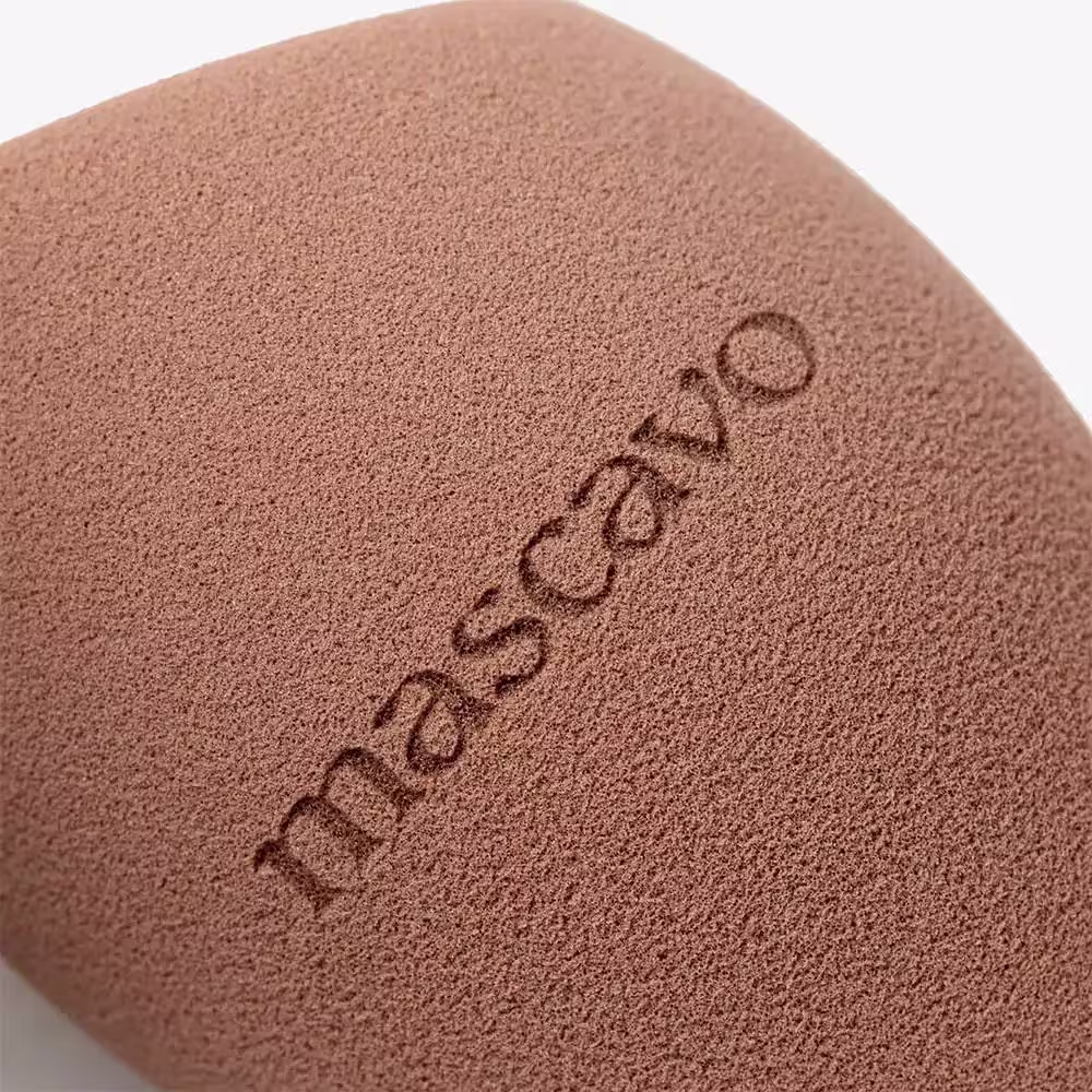 A imagem mostra detalhes da esponja ProBliender, trata-se de uma superfície de textura arenosa, com a inscrição "Mascavo" gravada na superfície. A cor predominante é um tom de bege claro.
