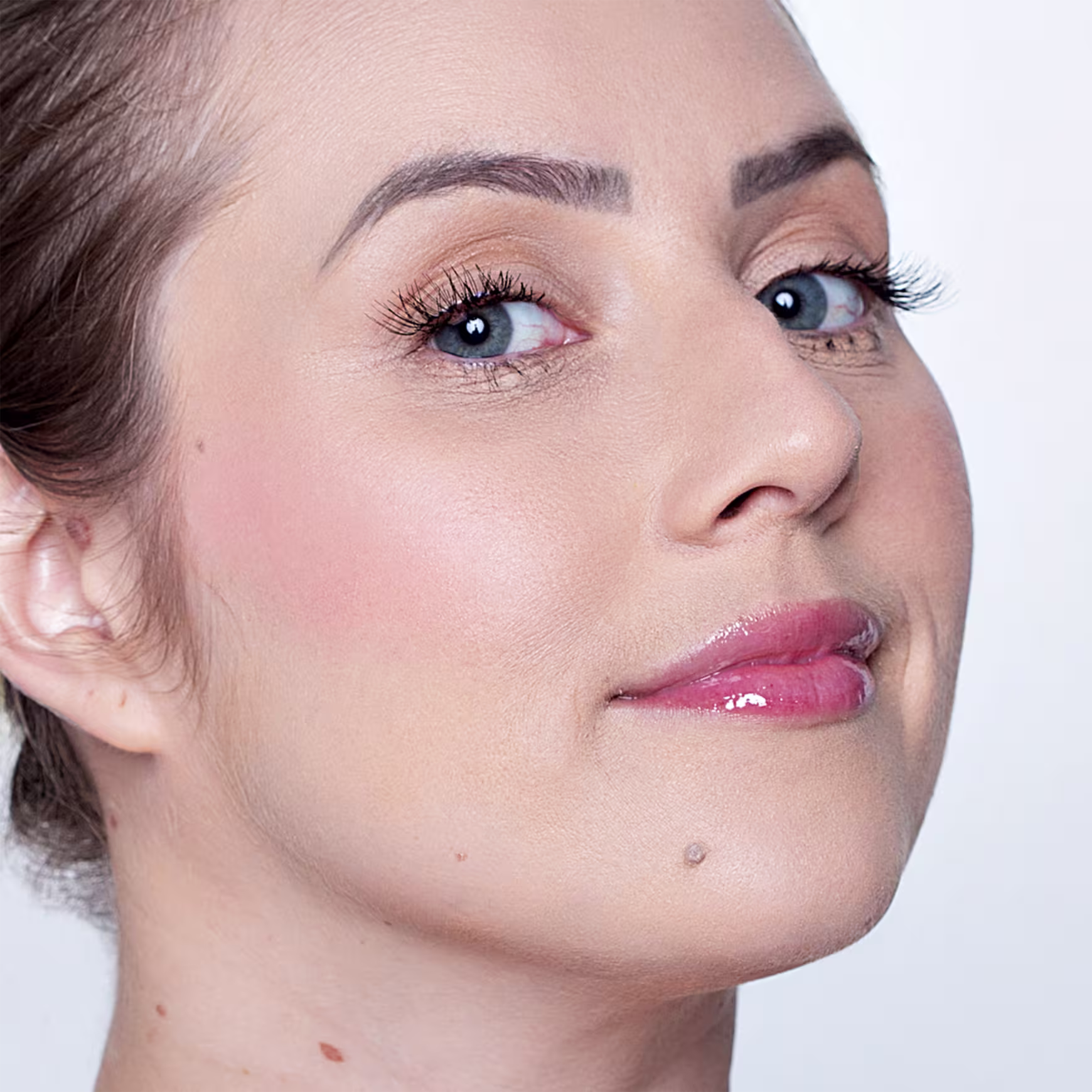 A imagem mostra um close-up em um rosto de uma mulher de pele clara. Ela está com uma maquiagem sutil, mostrando como o blush fica na pele.