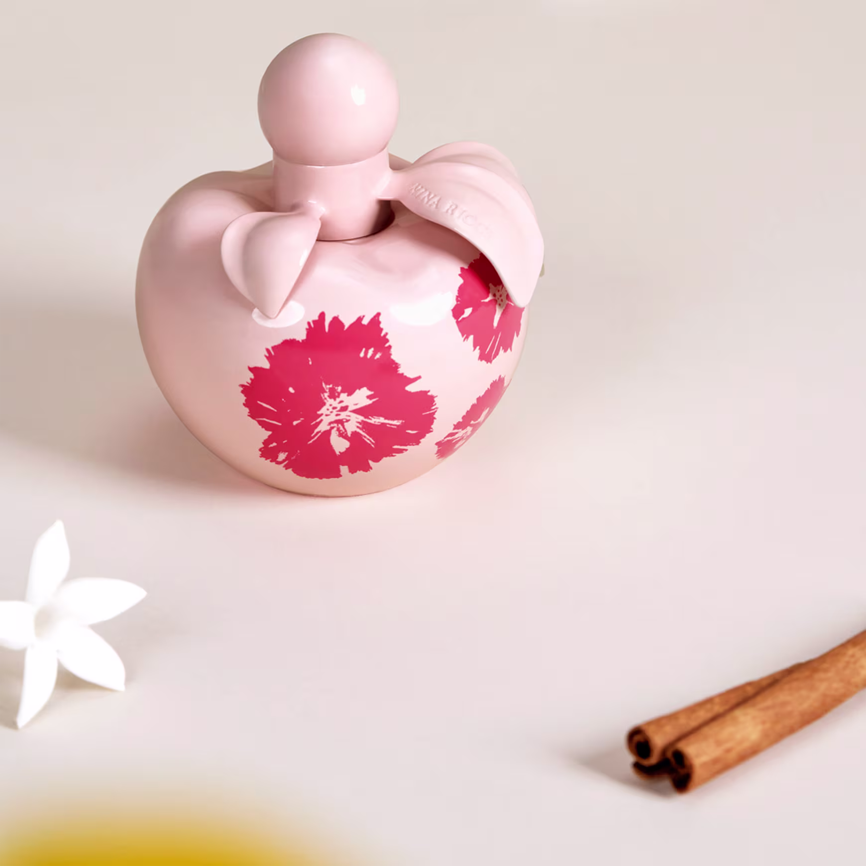 Conjunto de produtos Nina Ricci Nina Fleur. Frasco de perfume transparente em formato de coração com detalhes florais vermelhos. Loção corporal branca em tubo cilíndrico com o nome "Nina Fleur" impresso.