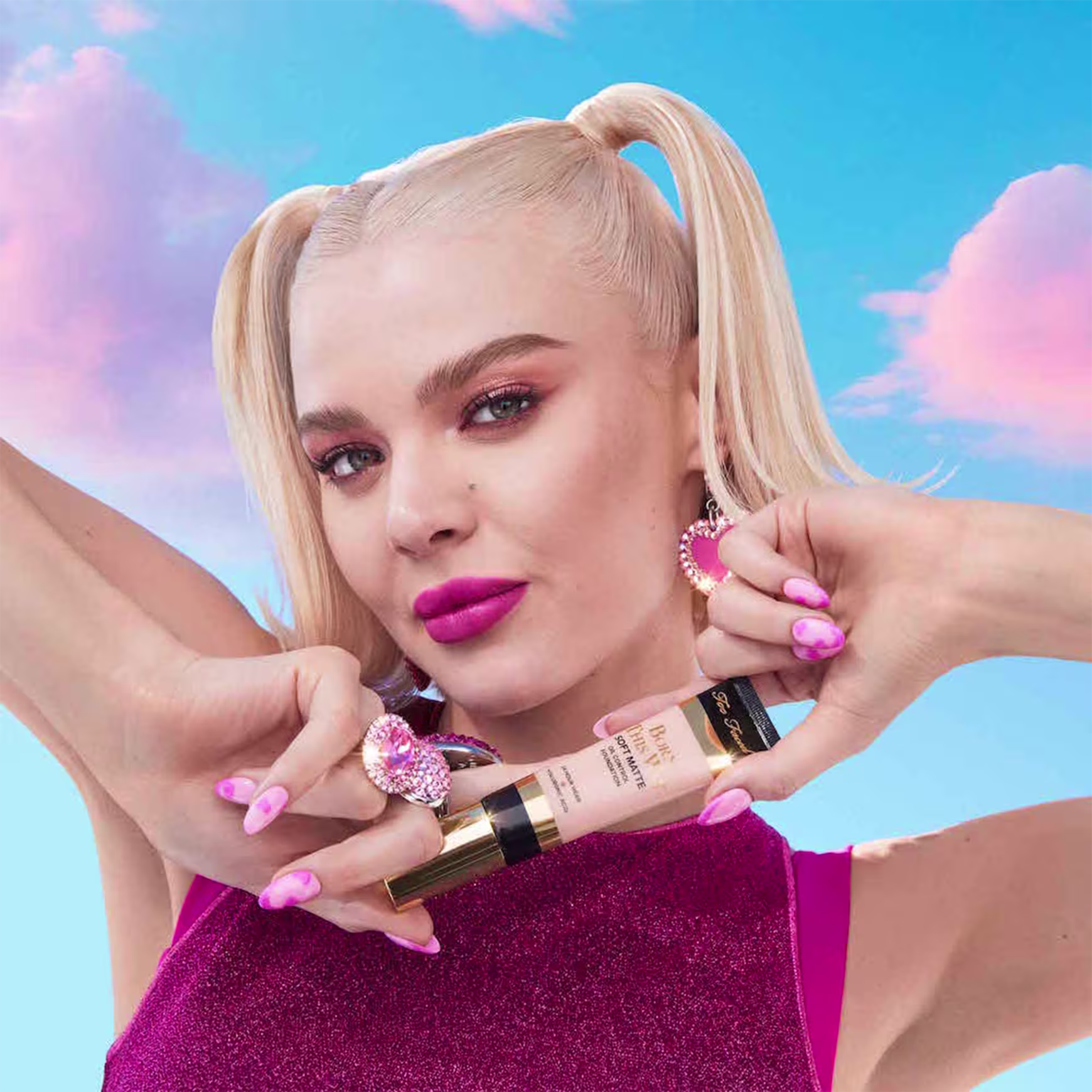 A imagem mostra uma mulher super produzida segurando uma embalagem da base próxima ao queixo.