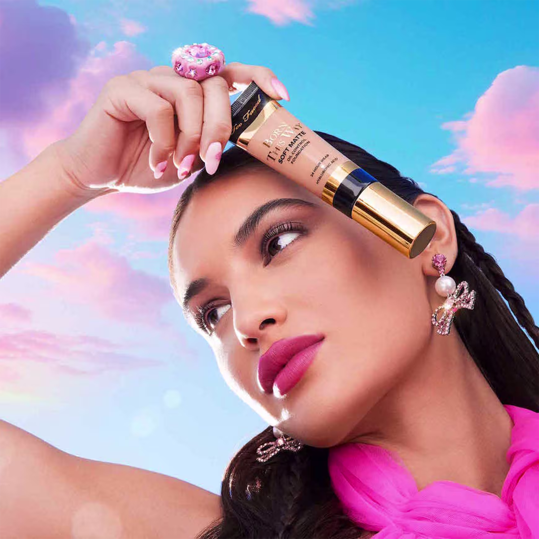 A imagem mostra uma mulher super produzida segurando uma embalagem da base próxima ao rosto.