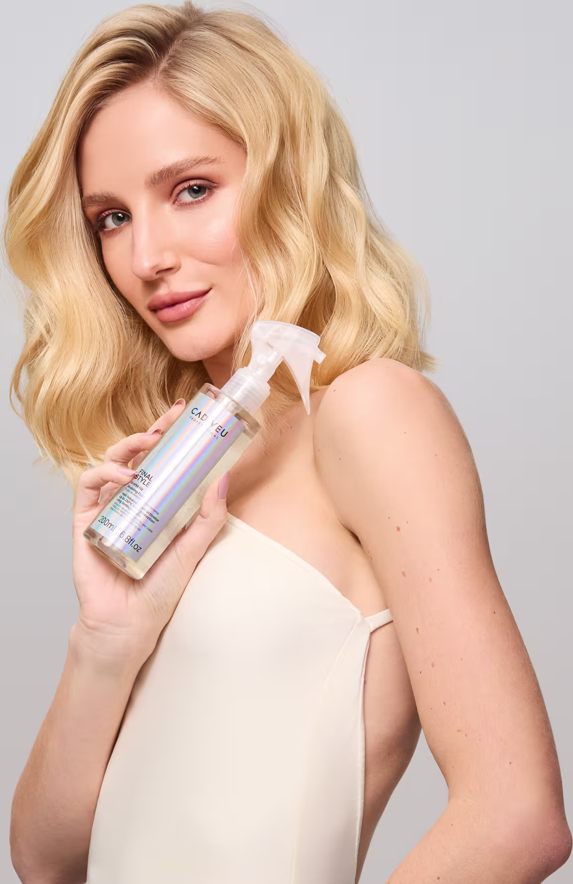 Esta imagem mostra uma mulher loira com cabelos ondulados na altura dos ombros, mostrando o produto Cadiveu Professional Final Style Shaper Fix.