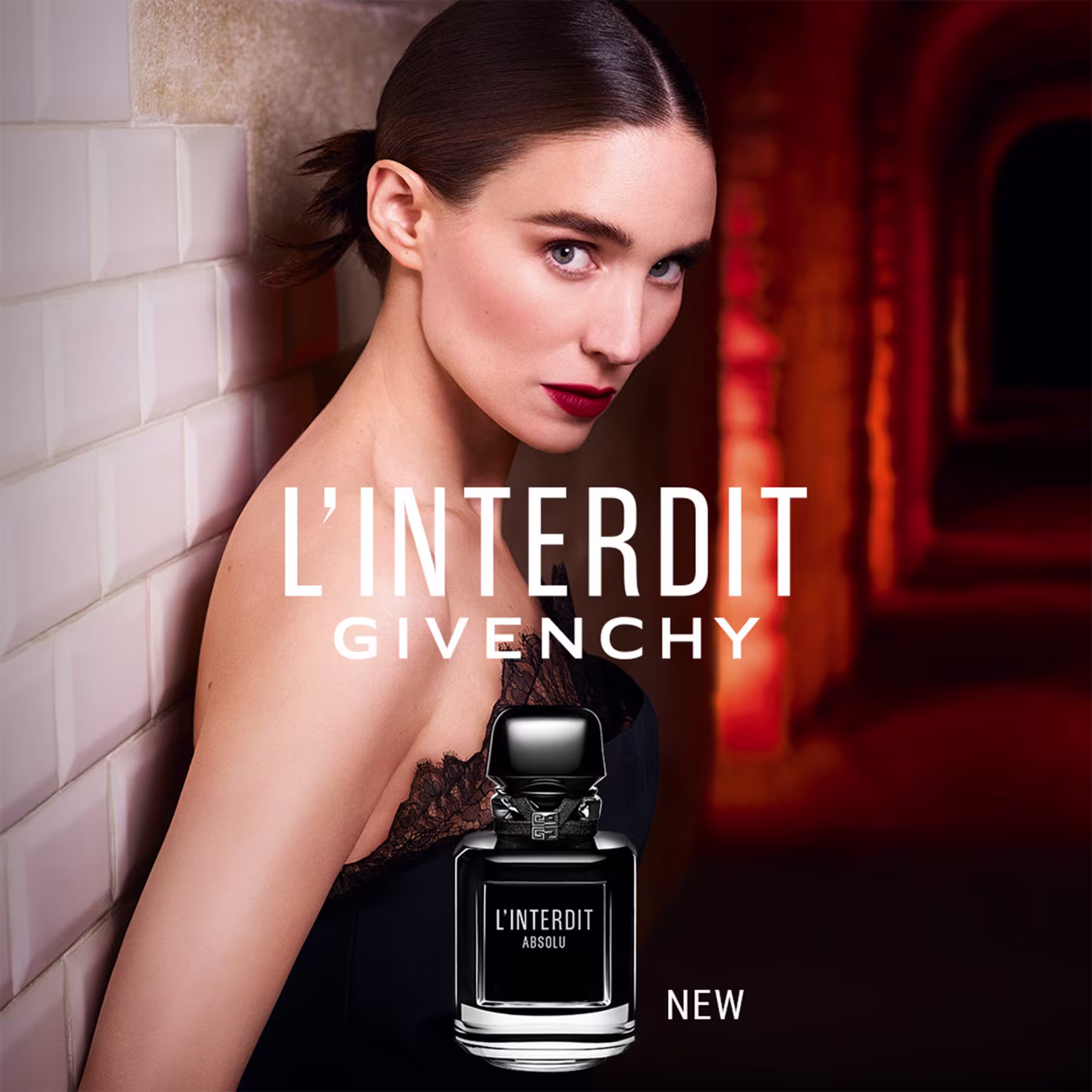 Esta imagem é um anúncio publicitário para o perfume e mostra uma bela modelo posando sensualmente com os cabelos pretos presos e maquiagem marcante, com batom vermelho. A sua frente tem o frasco e o nome do perfume "L'Interdit Absolu" da Givenchy.