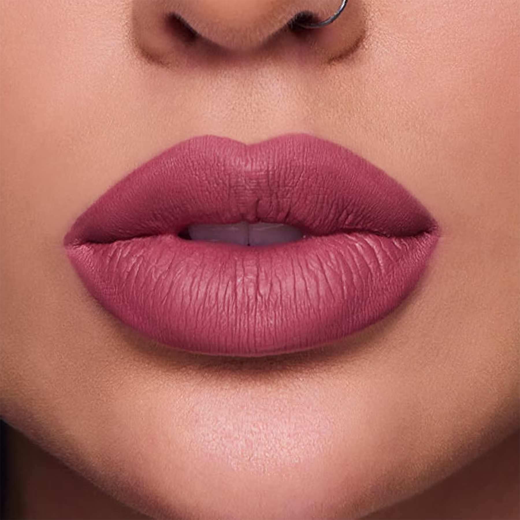 A imagem mostra um close nos lábios carnudos e bem delineados de uma mulher branca. Os lábios estão cobertos com o batom de tom rosa intenso e mate, que realça a textura e o volume natural dos lábios.