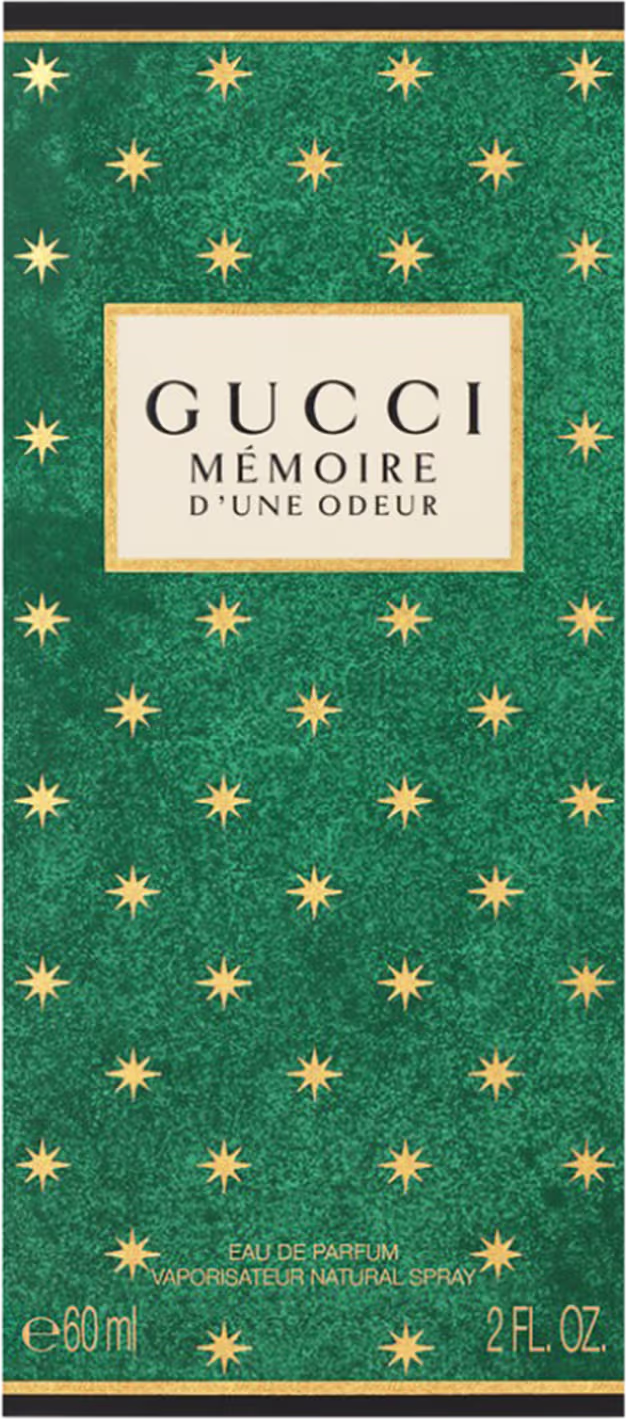 A imagem mostra uma caixa retangular em um fundo branco. A caixa é de cor verde com pequenas estrelas amarelas. Mais acima, uma etiqueta bege com o nome da marca e perfume e, no rodapé, informações de tipo de concentração e volumetria.