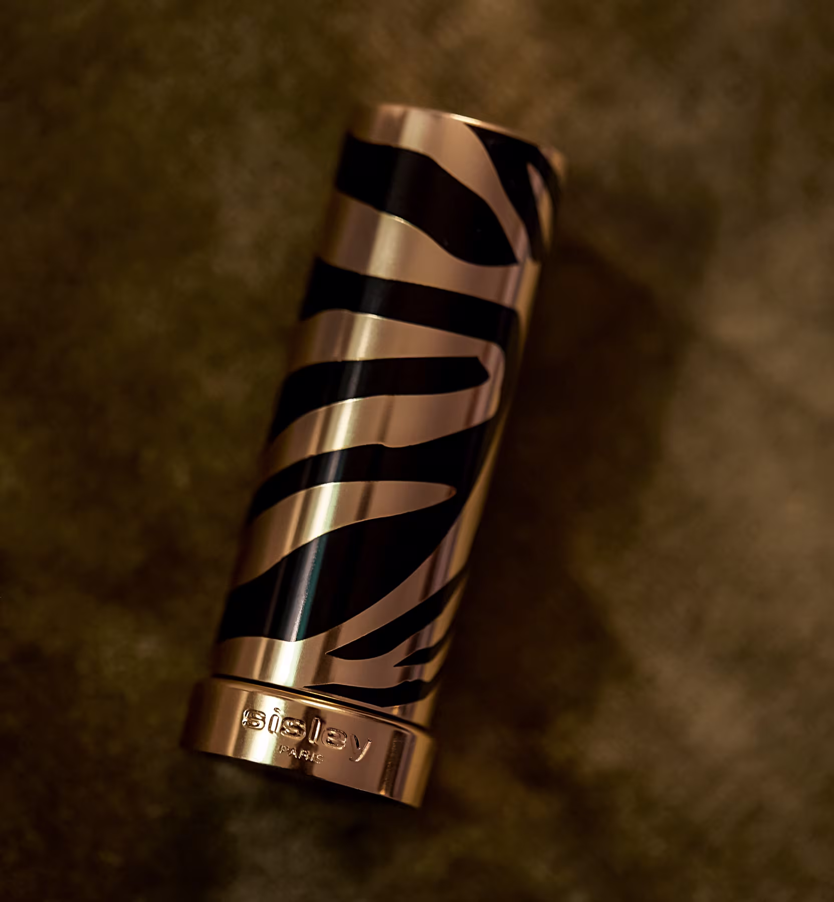 A imagem mostra o batom fechado, em um fundo dourado com detalhes escuros.