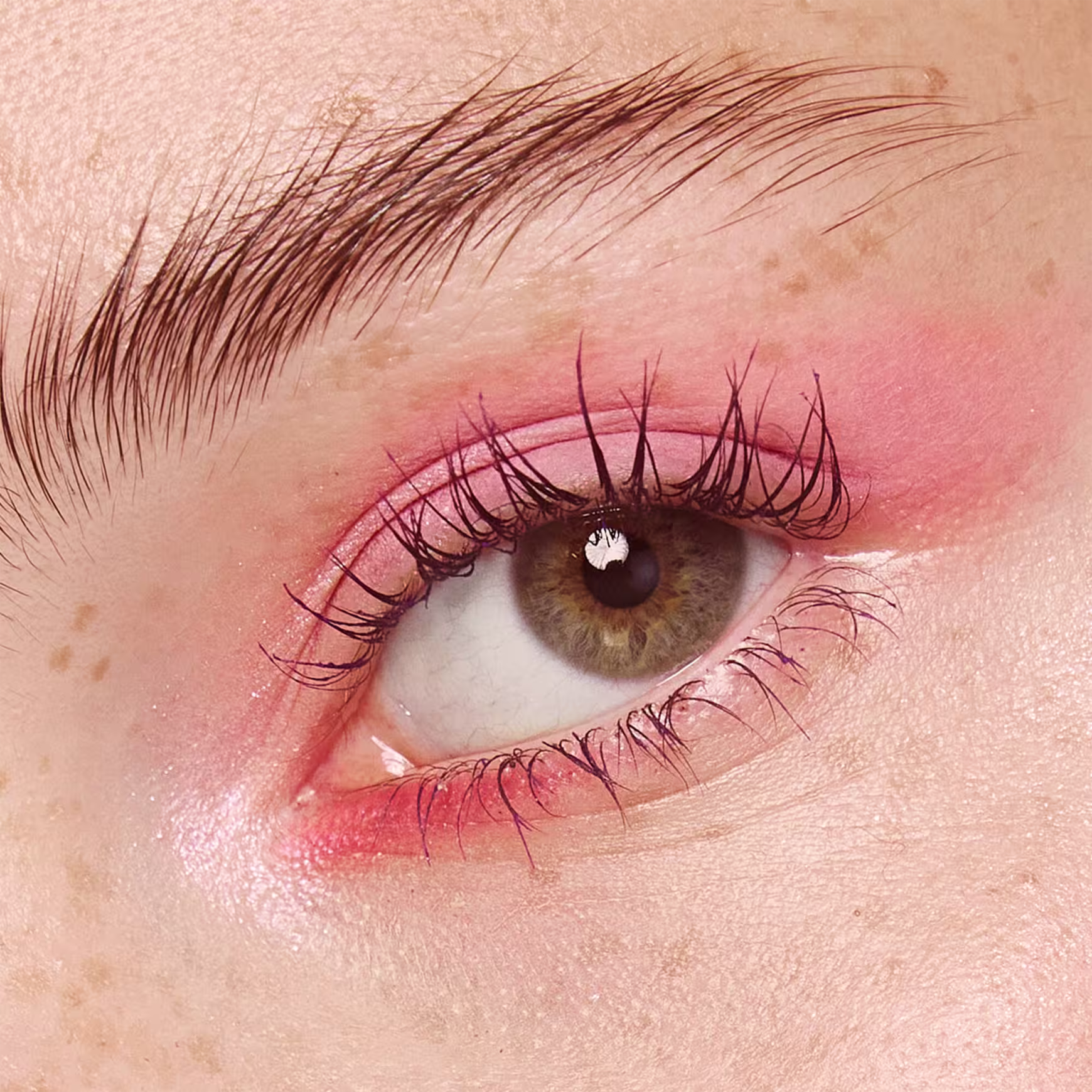 A foto mostra um rosto feminino branco aproximado, com foco no olho verde. A pálpebra está pintada com uma sombra  rosa claro e os cílios bem definidos e alongados.
