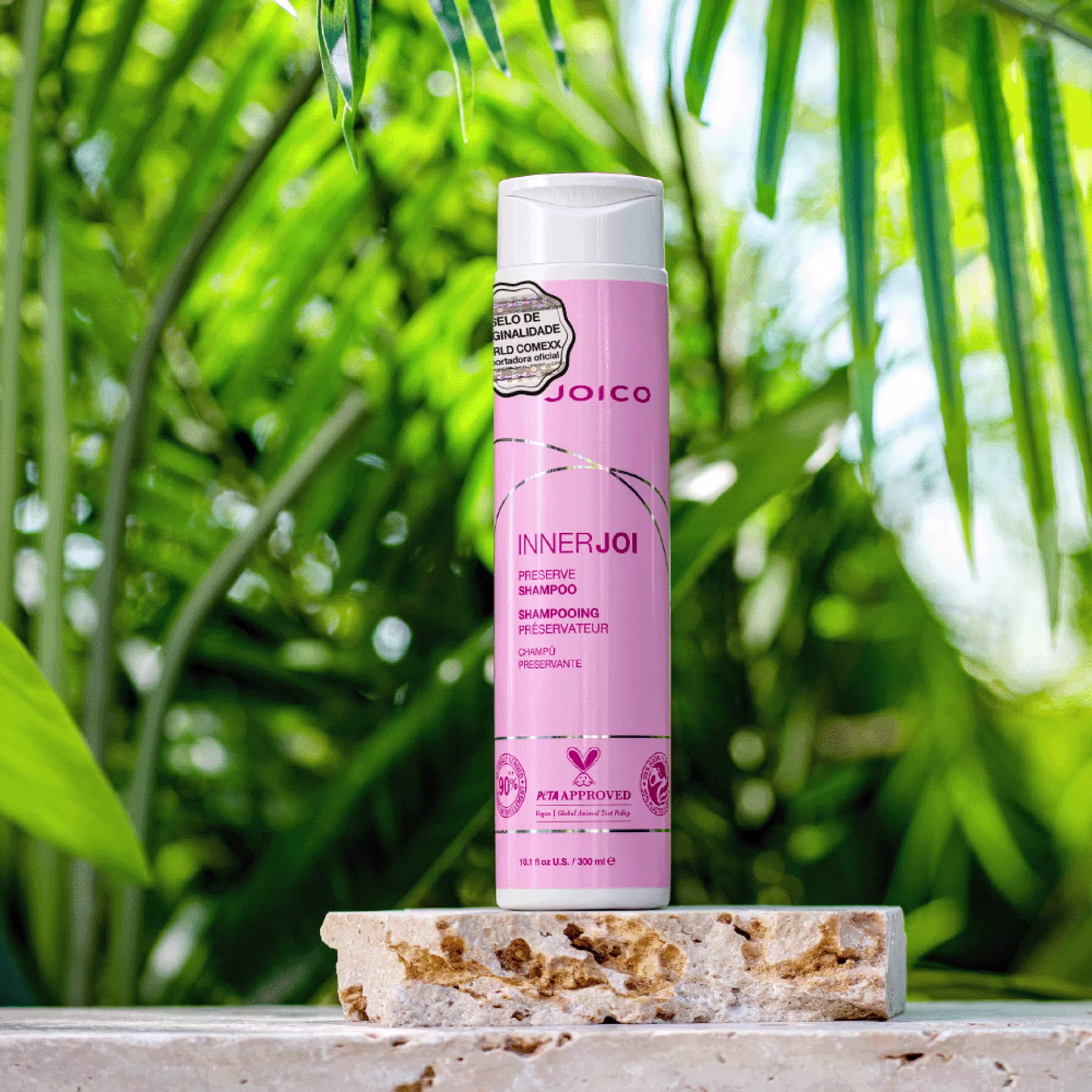 Ao centro, o Shampoo Joico InnerJoi Preserve (300ml) se destaca apoiado sobre uma pedra. O fundo da imagem, que remete à natureza, com folhas verdes, reforça a proposta da linha.