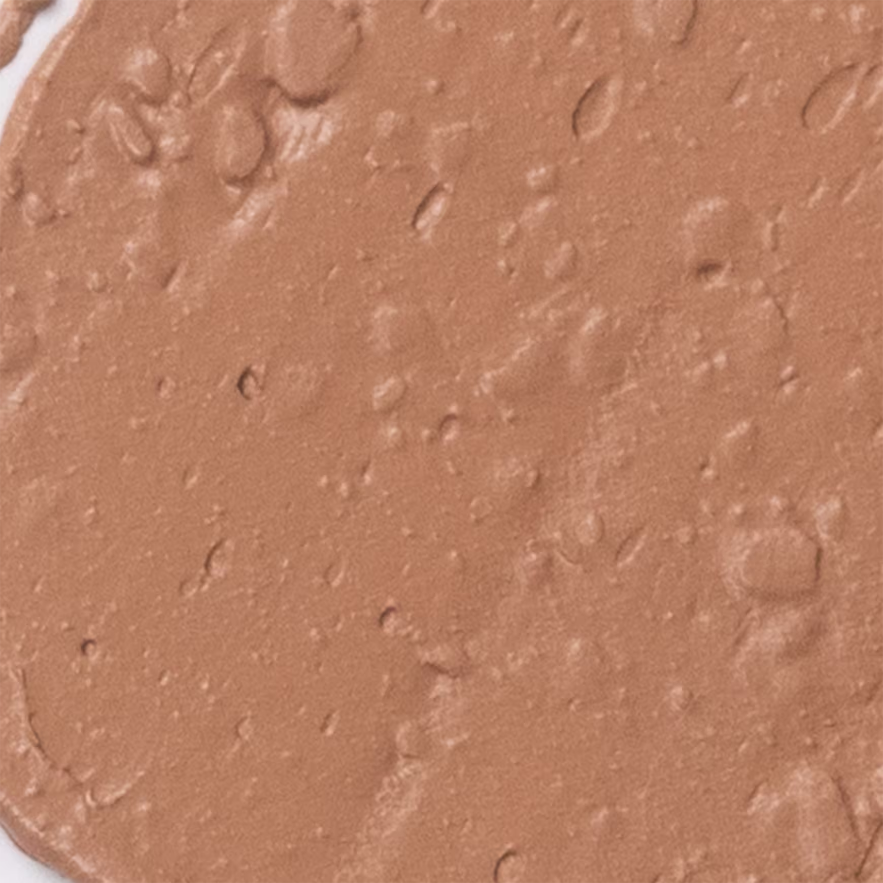 A imagem apresenta detalha da textura da base Océane Edition Foundation Stick. A superfície apresenta uma tonalidade bege escuro e textura em bastão cremosa.