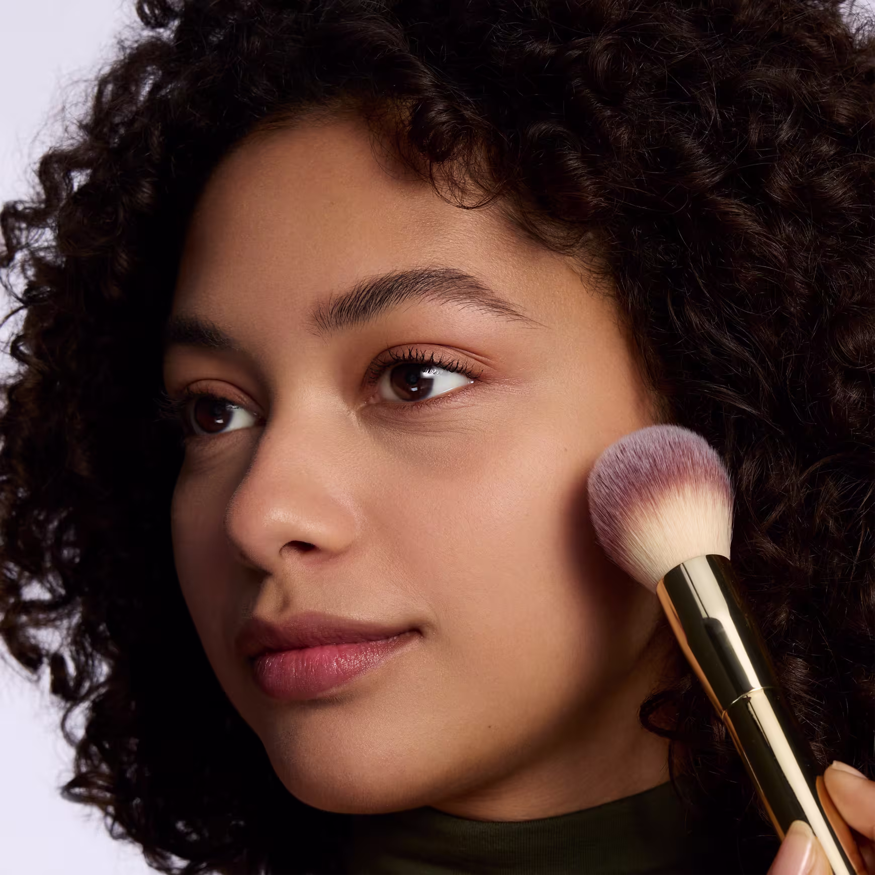 Modelo sorri enquanto aplica o pó solto com um pincel na face.