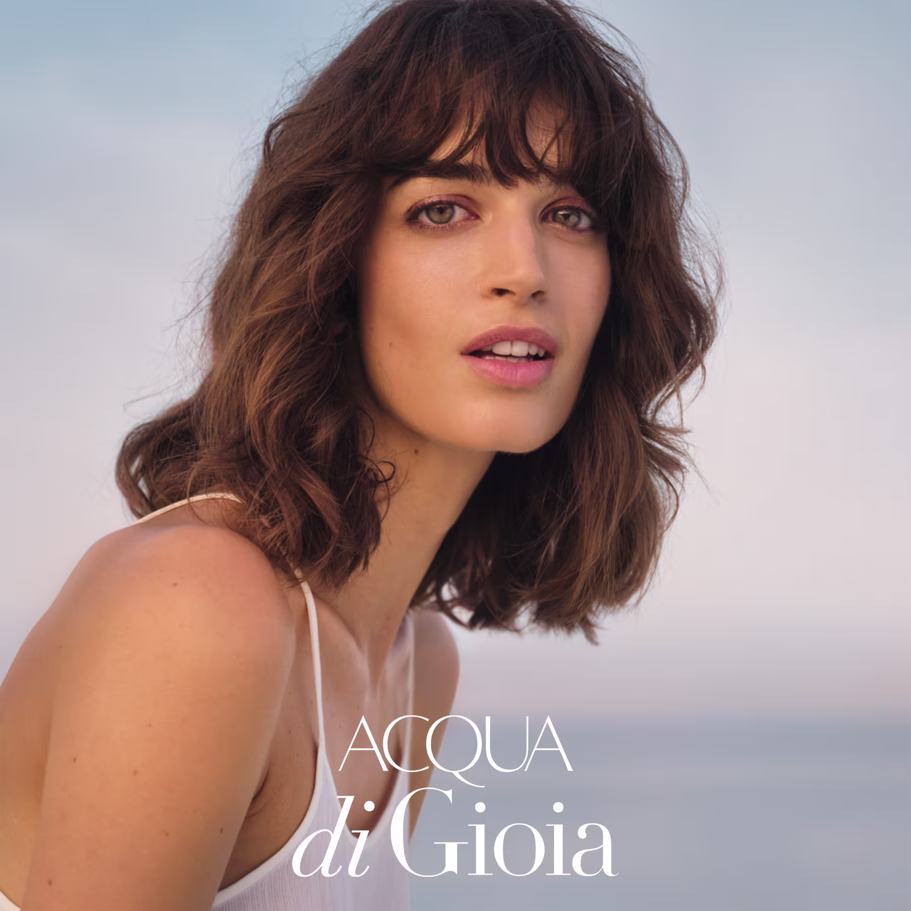 Uma modelo jovem de cabelo castanho escuro na altura do ombro sorri com uma expressão serena.