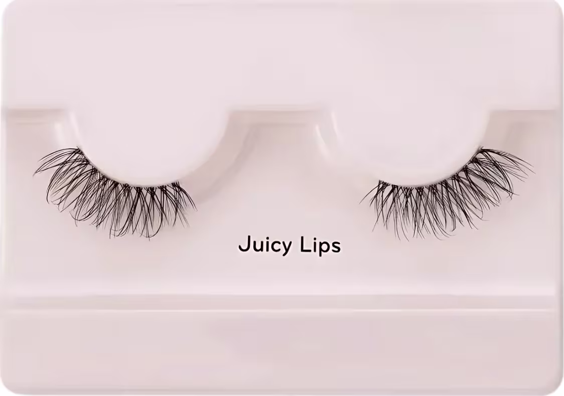 A imagem mostra os cílios postiços em um estojo plástico claro. O estojo tem uma cor nude claro e exibe um par de cílios postiços pretos.