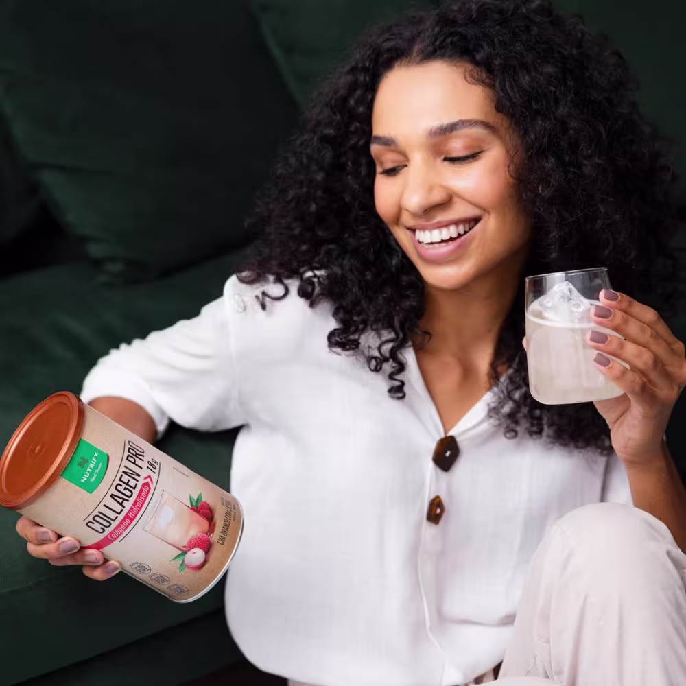 Uma modelo segurando a lata do suplemento e um copo, também com o suplemento.