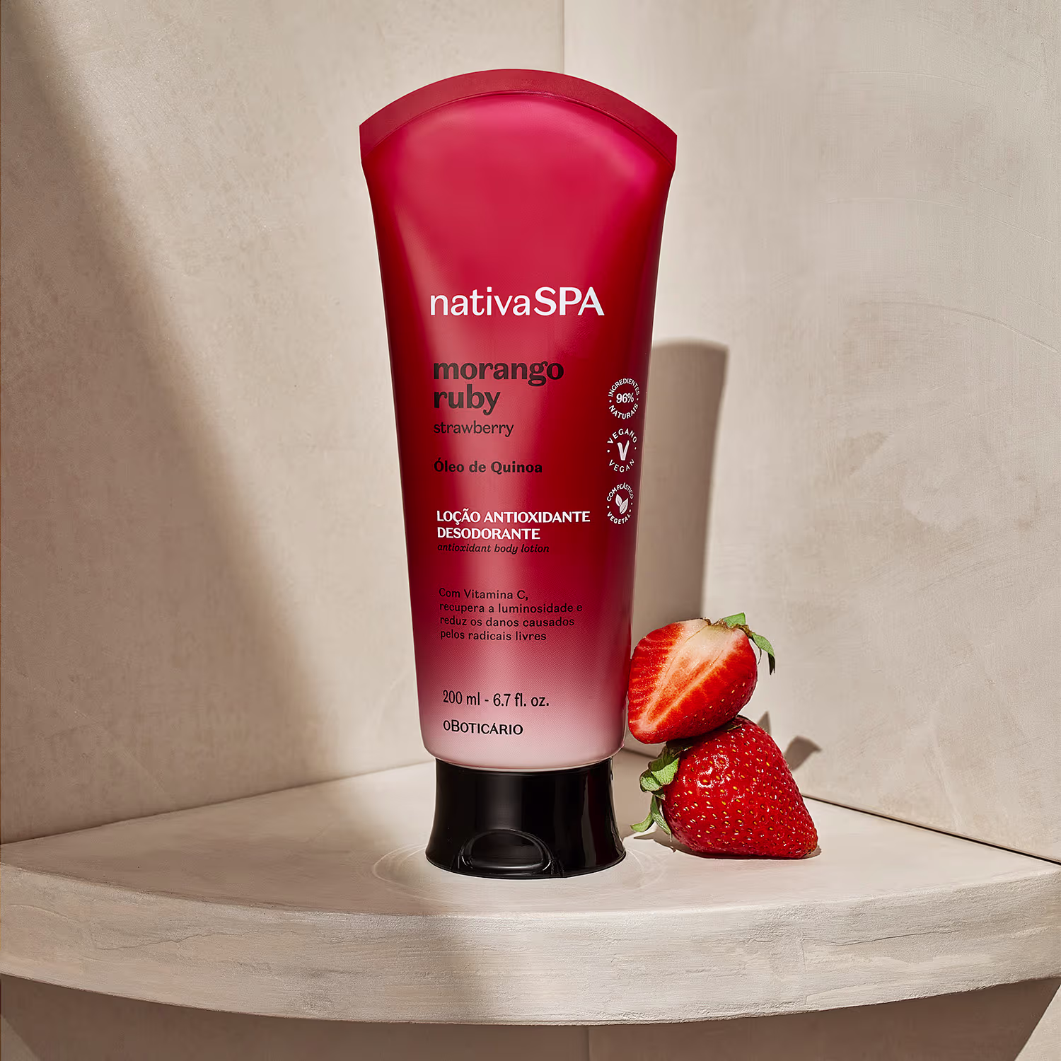 Embalagem plástica vermelha com detalhes em preto. Rótulo em português com informações sobre o produto, como "Óleo de Quinoa" e "Com Vitamina C". Tubo de 200 ml. Dois morangos frescos ao lado, complementando o tema da fragrância.