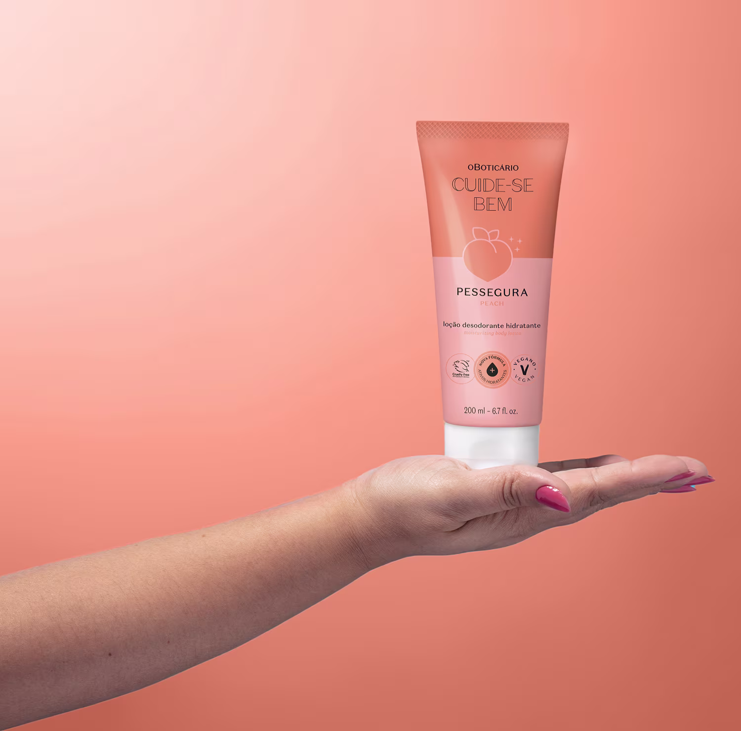 Loção corporal em um tubo plástico perolado na cor salmão. O tubo tem 200 ml e está sendo segurado por uma mão feminina com esmalte rosa nas unhas. O rótulo exibe o nome do produto "Cuide-se Bem" da marca "Pessegura". O fundo é em tom coral.